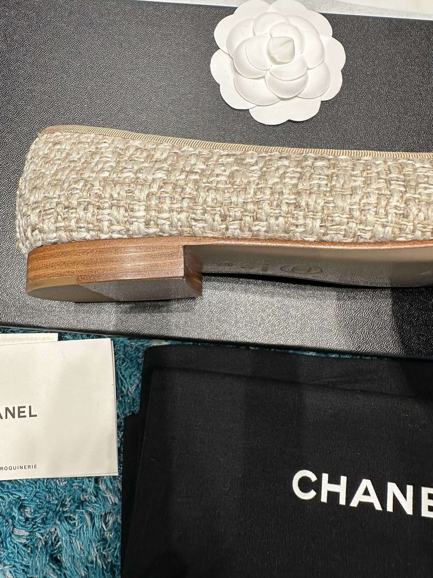 A pair of Chanel beige tweed ballet flats with a leather toe cap featuring the stitched CC logo and a small bow, presented in their original luxury packaging. - Hình 7