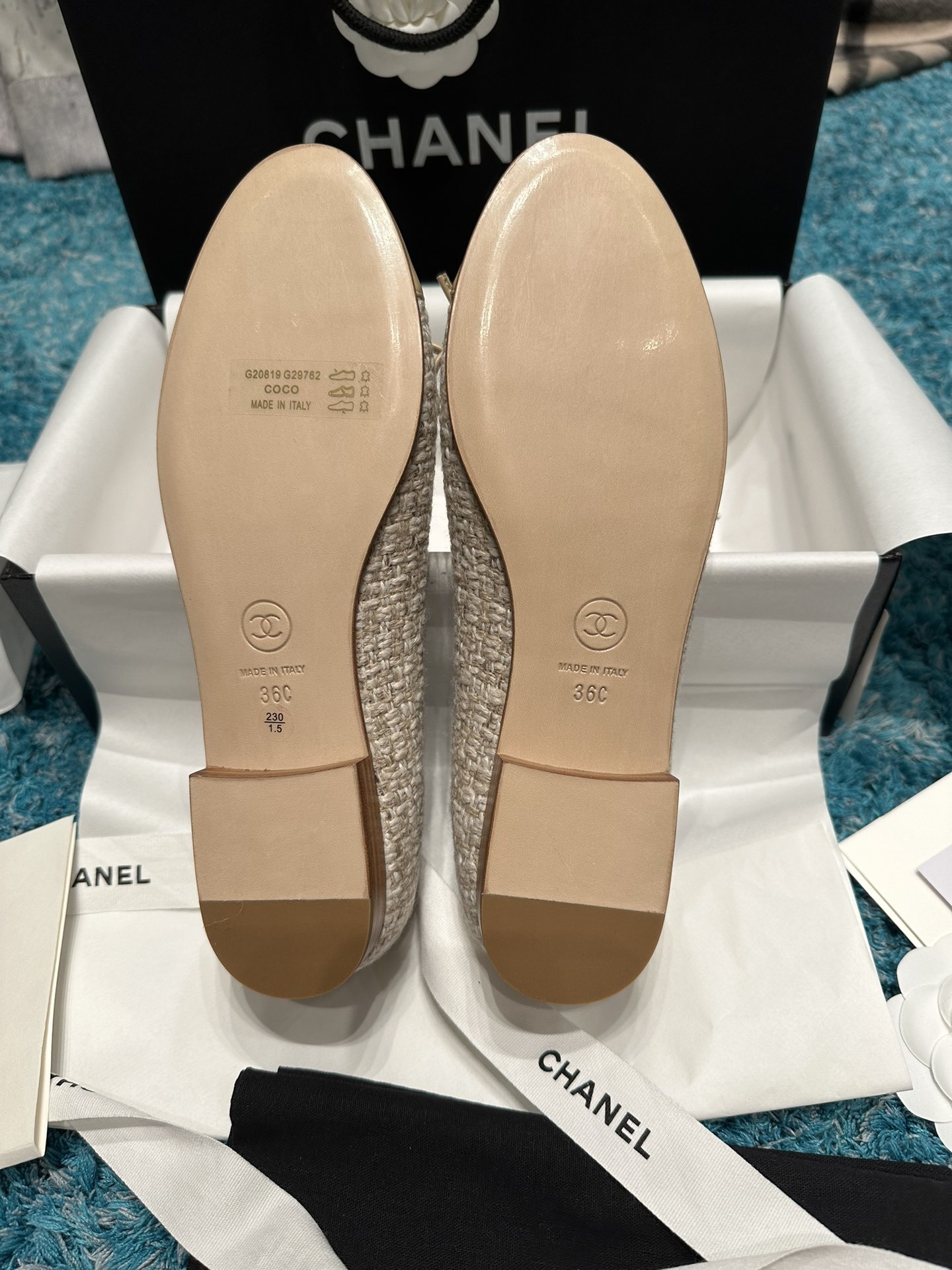 A pair of Chanel beige tweed ballet flats with a leather toe cap featuring the stitched CC logo and a small bow, presented in their original luxury packaging. - Hình 5