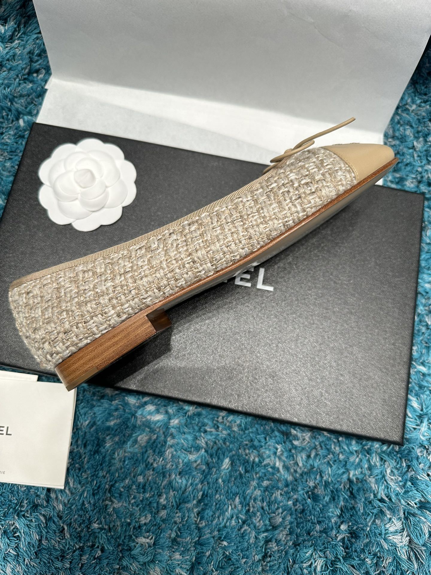 A pair of Chanel beige tweed ballet flats with a leather toe cap featuring the stitched CC logo and a small bow, presented in their original luxury packaging. - Hình 3