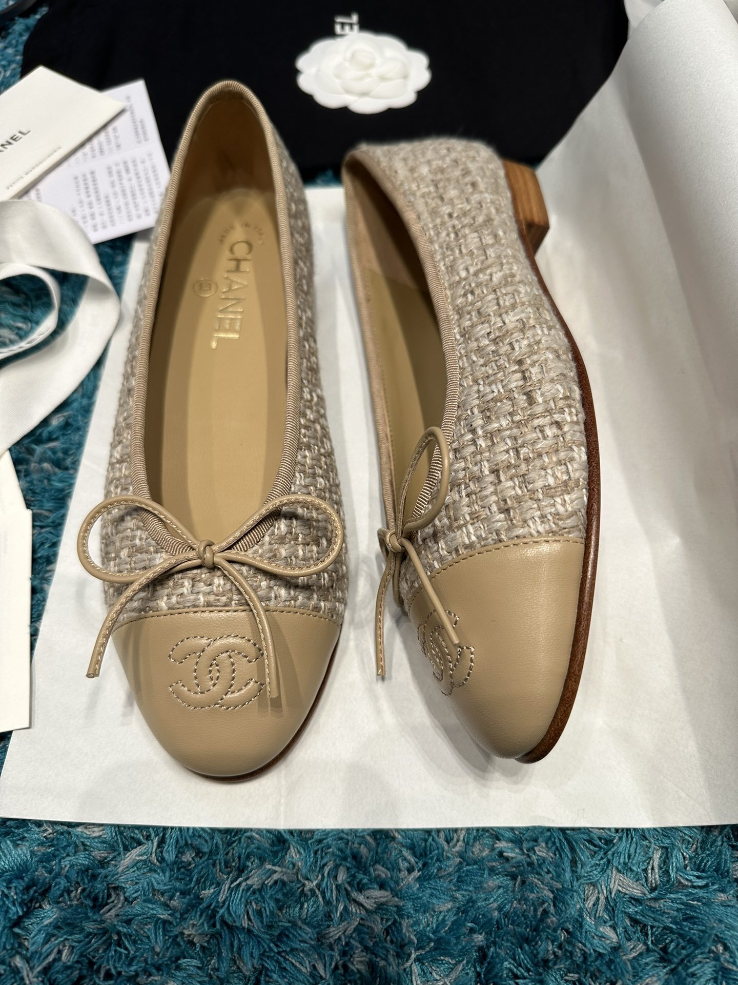 A pair of Chanel beige tweed ballet flats with a leather toe cap featuring the stitched CC logo and a small bow, presented in their original luxury packaging. - Hình 2