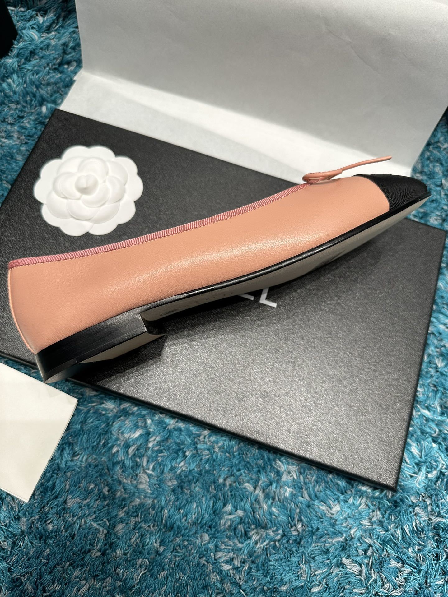 A pair of pink Chanel ballerina flats with black toe caps and bow details sitting in original packaging. - Hình 4