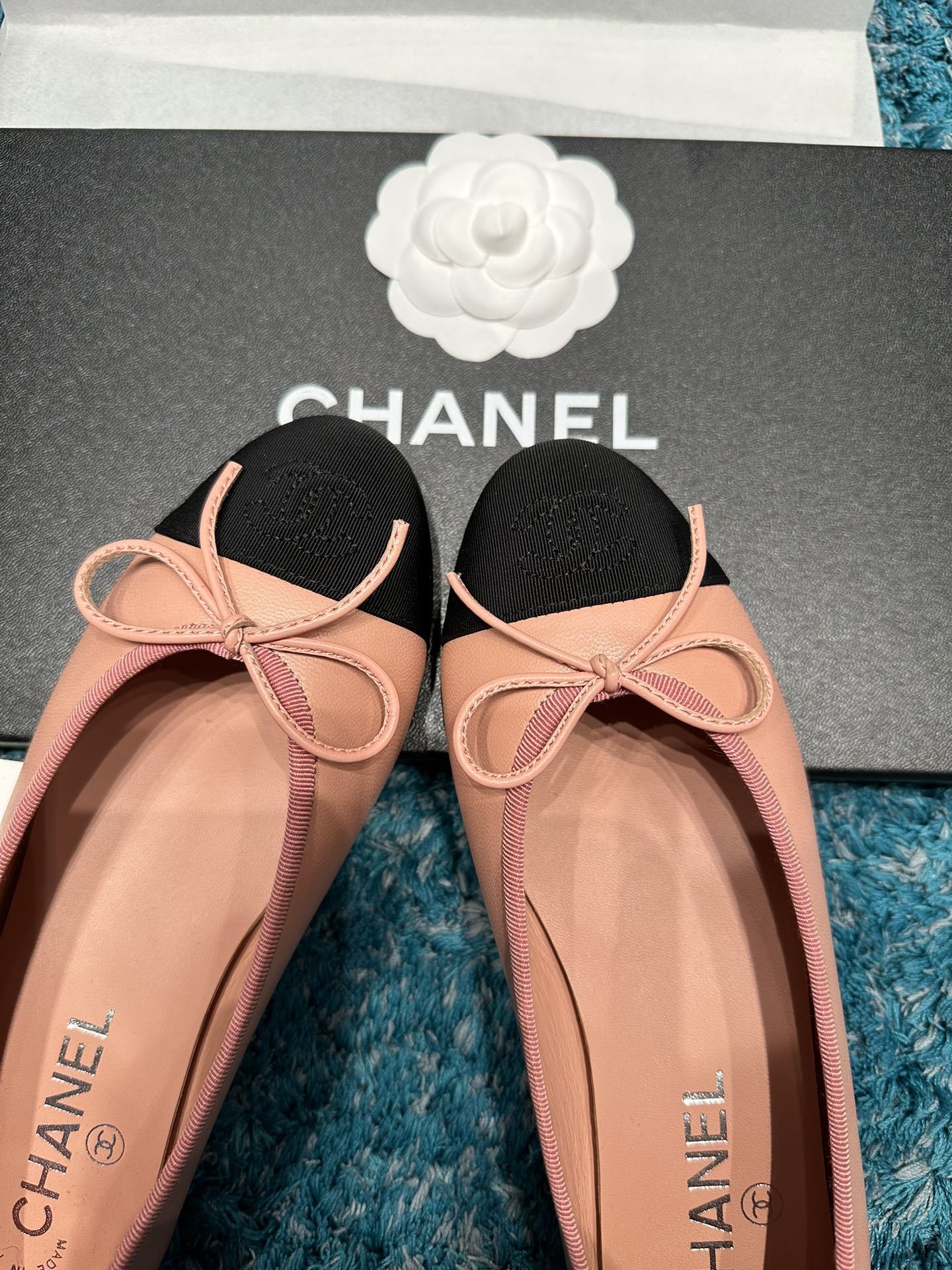 A pair of pink Chanel ballerina flats with black toe caps and bow details sitting in original packaging. - Hình 3