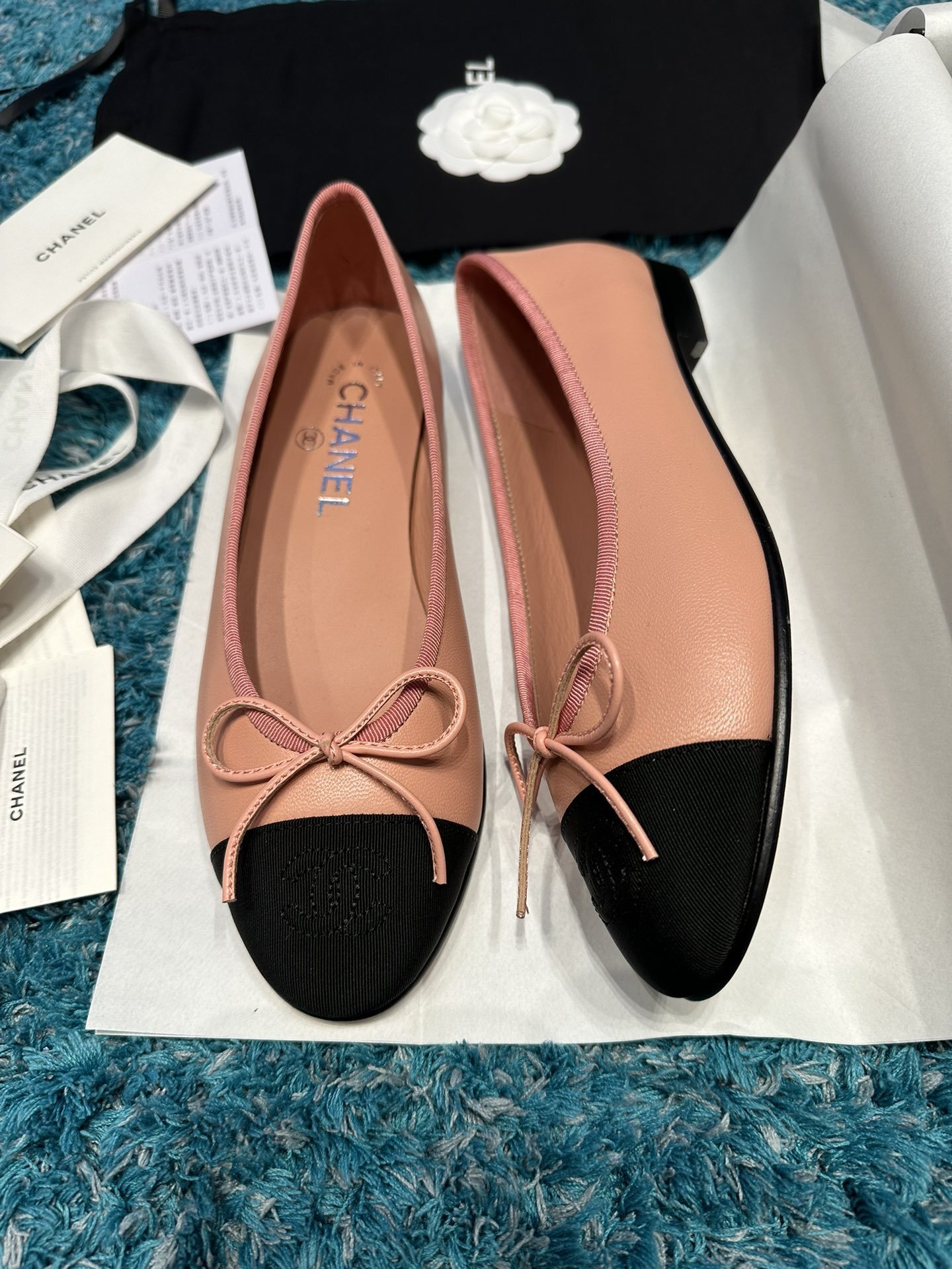 A pair of pink Chanel ballerina flats with black toe caps and bow details sitting in original packaging. - Hình 2