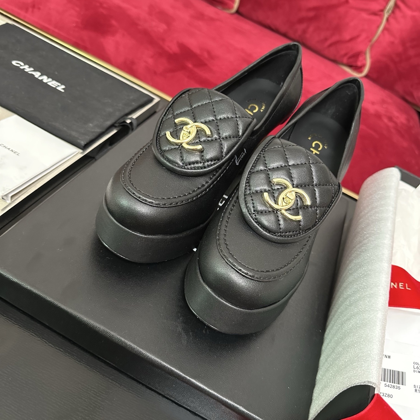 Chanel black quilted leather platform loafers with gold CC logo hardware on a display table with original packaging. - Hình 2