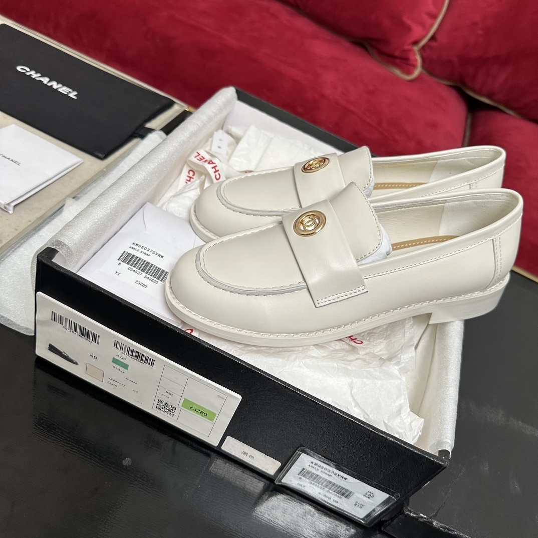 A pair of luxury Chanel white leather loafers with gold CC logo hardware displayed in their original black and white box with authenticity cards. - Hình 2