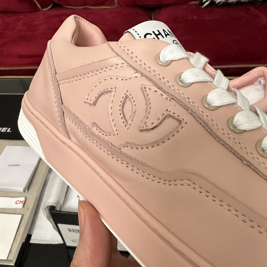 A pair of pink Chanel leather low-top sneakers with white laces and embossed CC logo sitting in their original box with accessories. - Hình 7
