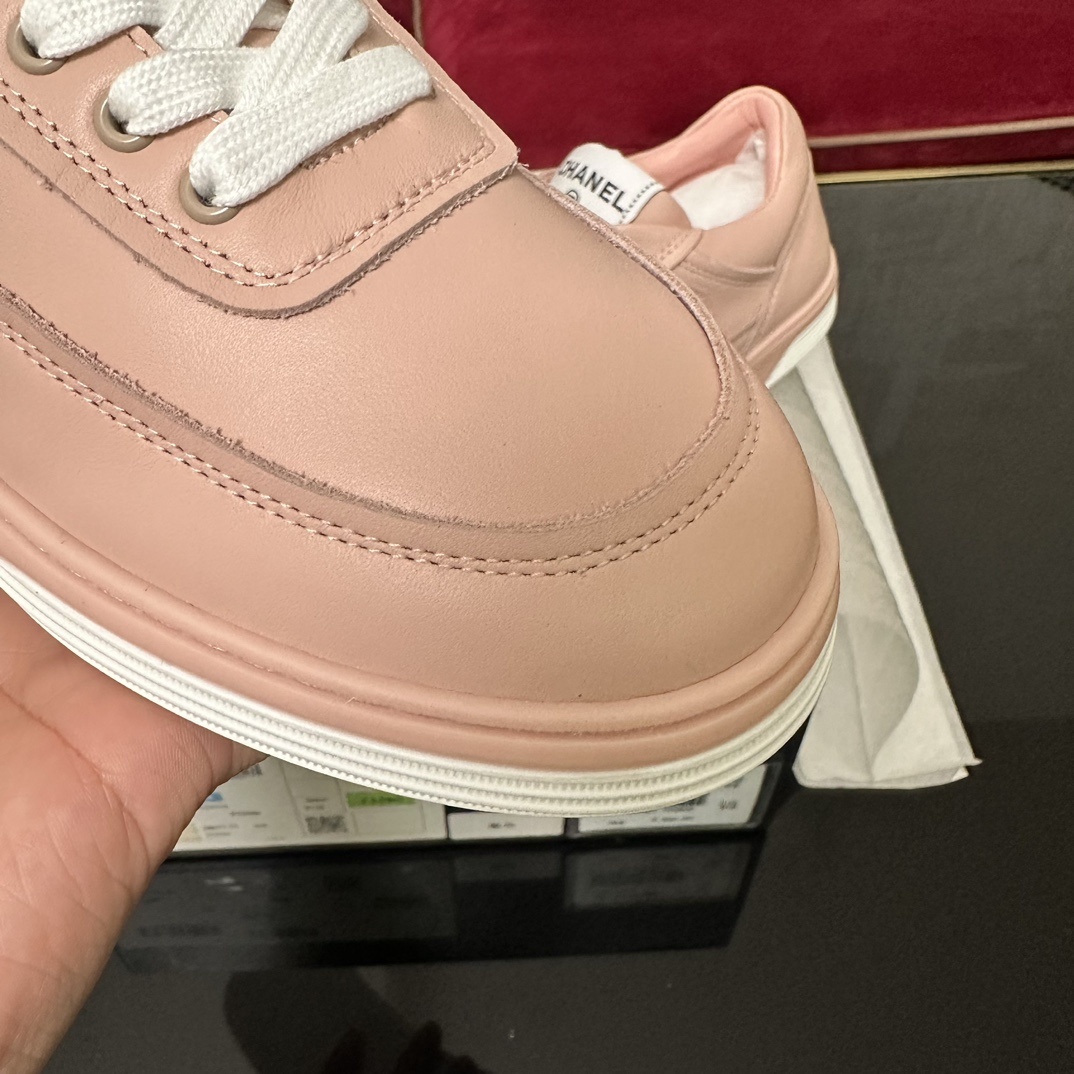 A pair of pink Chanel leather low-top sneakers with white laces and embossed CC logo sitting in their original box with accessories. - Hình 6