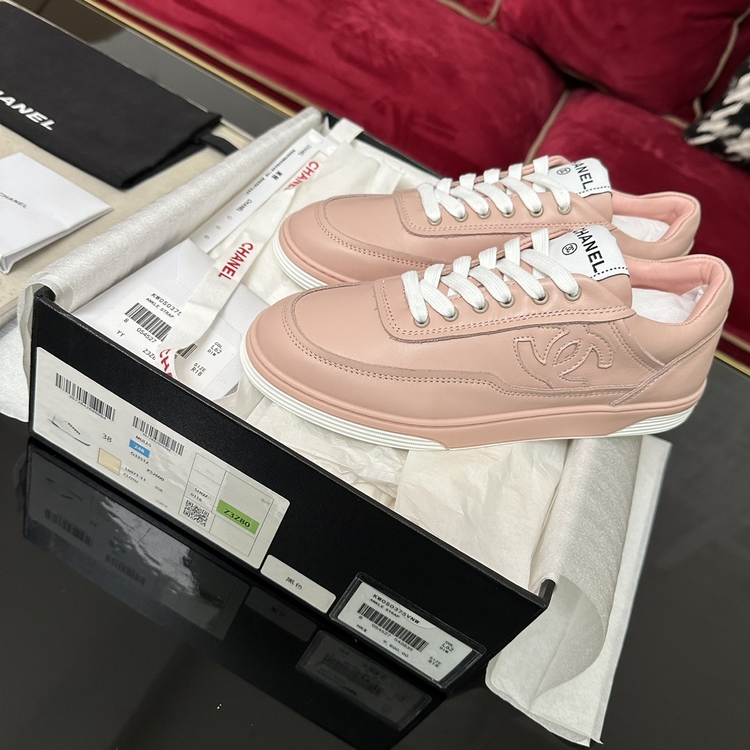 A pair of pink Chanel leather low-top sneakers with white laces and embossed CC logo sitting in their original box with accessories. - Hình 2