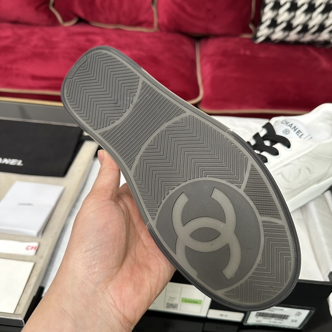 Premium white Chanel low-top leather sneakers with black laces and embossed CC logo, displayed with original luxury packaging. - Hình 9