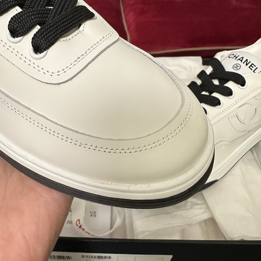 Premium white Chanel low-top leather sneakers with black laces and embossed CC logo, displayed with original luxury packaging. - Hình 6