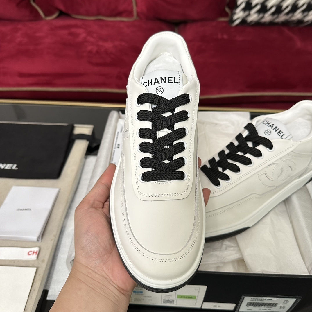 Premium white Chanel low-top leather sneakers with black laces and embossed CC logo, displayed with original luxury packaging. - Hình 3