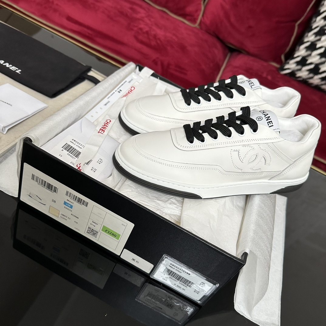 Premium white Chanel low-top leather sneakers with black laces and embossed CC logo, displayed with original luxury packaging. - Hình 2