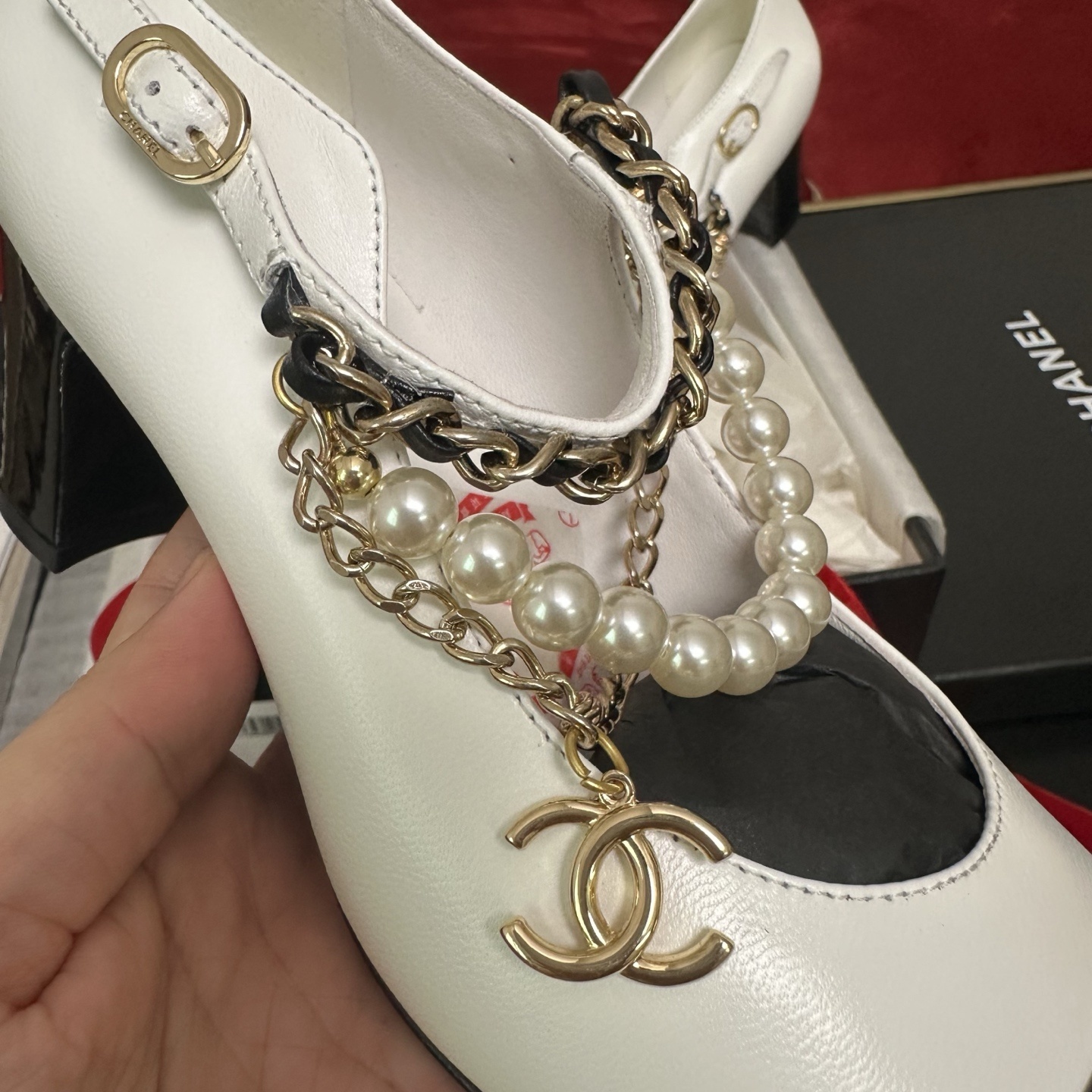 Pair of white Chanel Mary Jane pumps with black patent leather cap toes and decorative pearl and gold chain ankle straps in a luxury box. - Hình 7