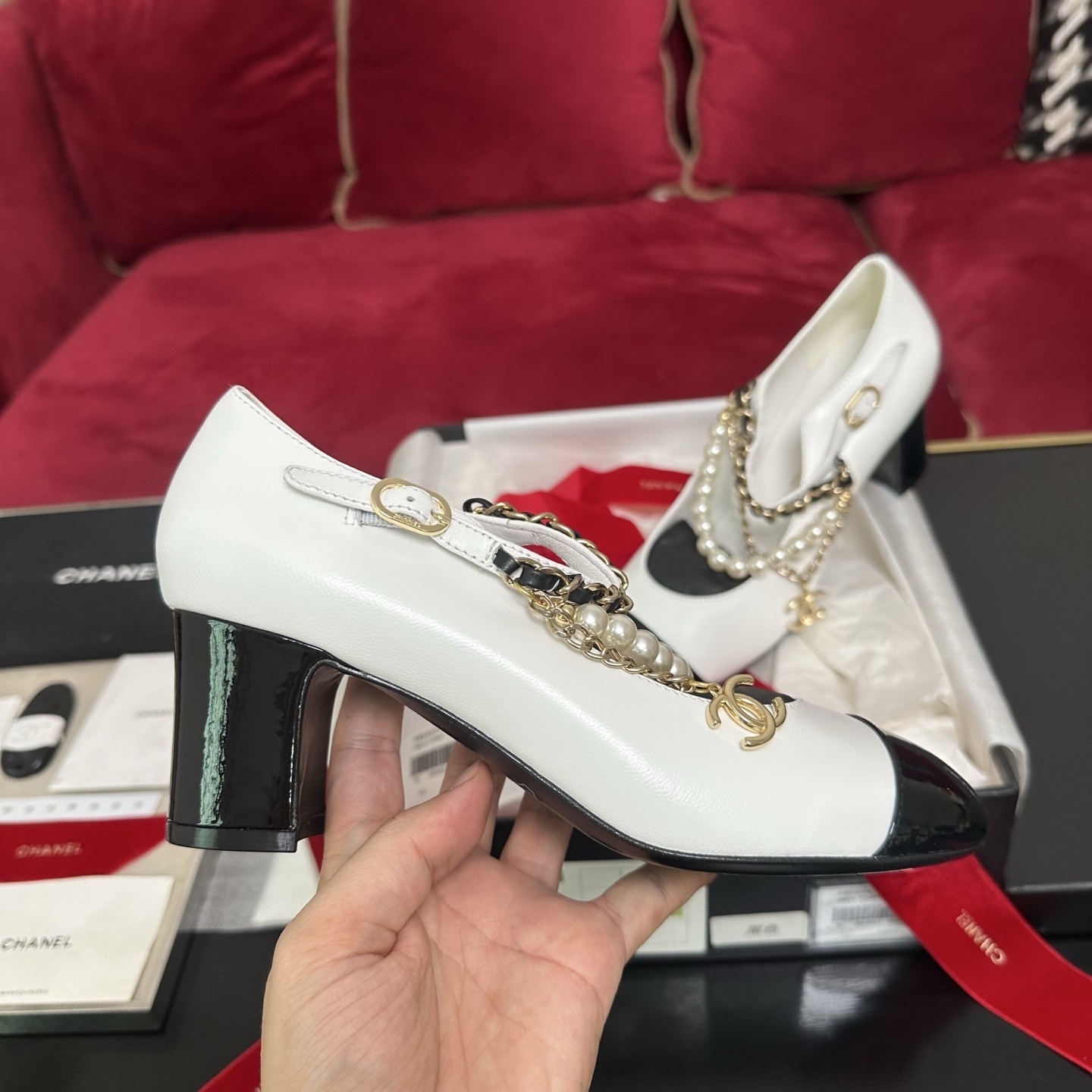Pair of white Chanel Mary Jane pumps with black patent leather cap toes and decorative pearl and gold chain ankle straps in a luxury box. - Hình 5