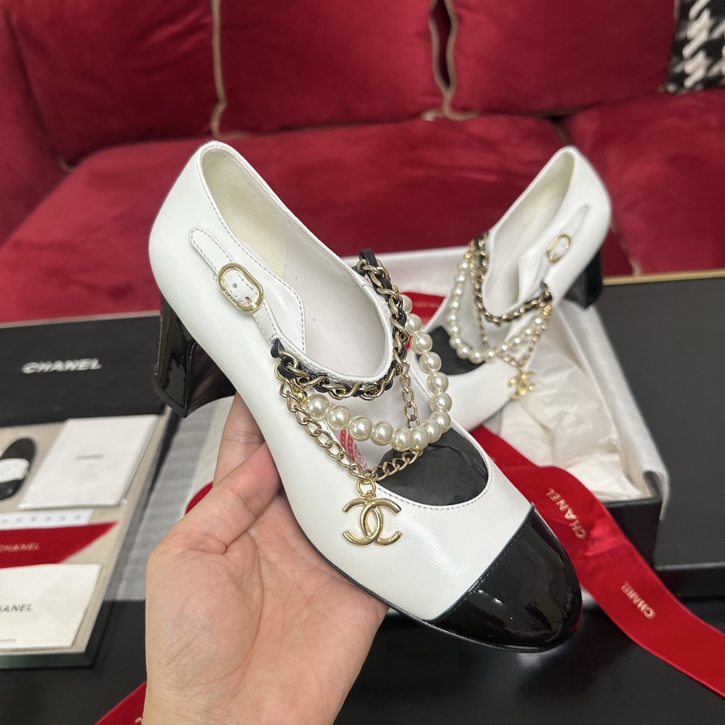 Pair of white Chanel Mary Jane pumps with black patent leather cap toes and decorative pearl and gold chain ankle straps in a luxury box. - Hình 4