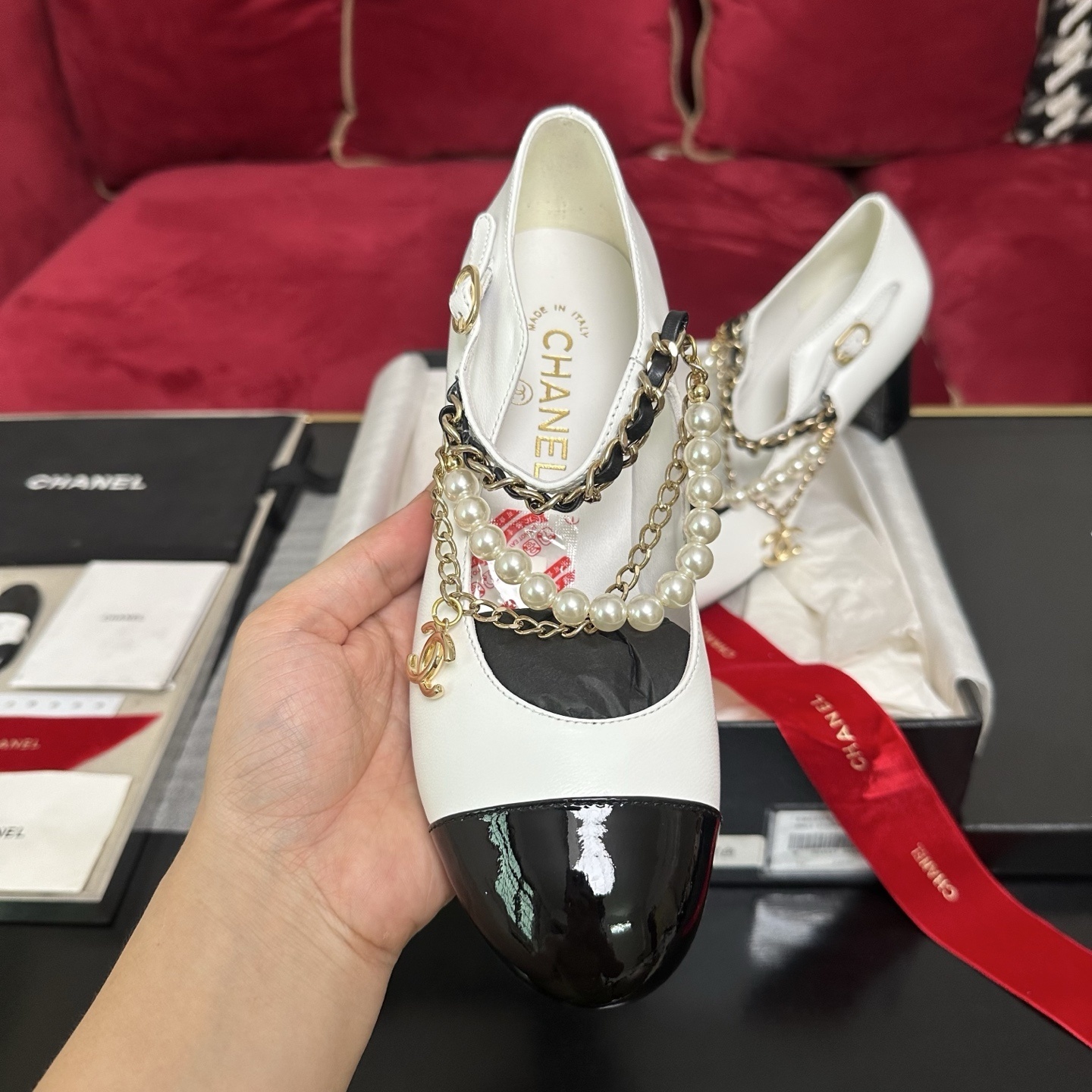 Pair of white Chanel Mary Jane pumps with black patent leather cap toes and decorative pearl and gold chain ankle straps in a luxury box. - Hình 3