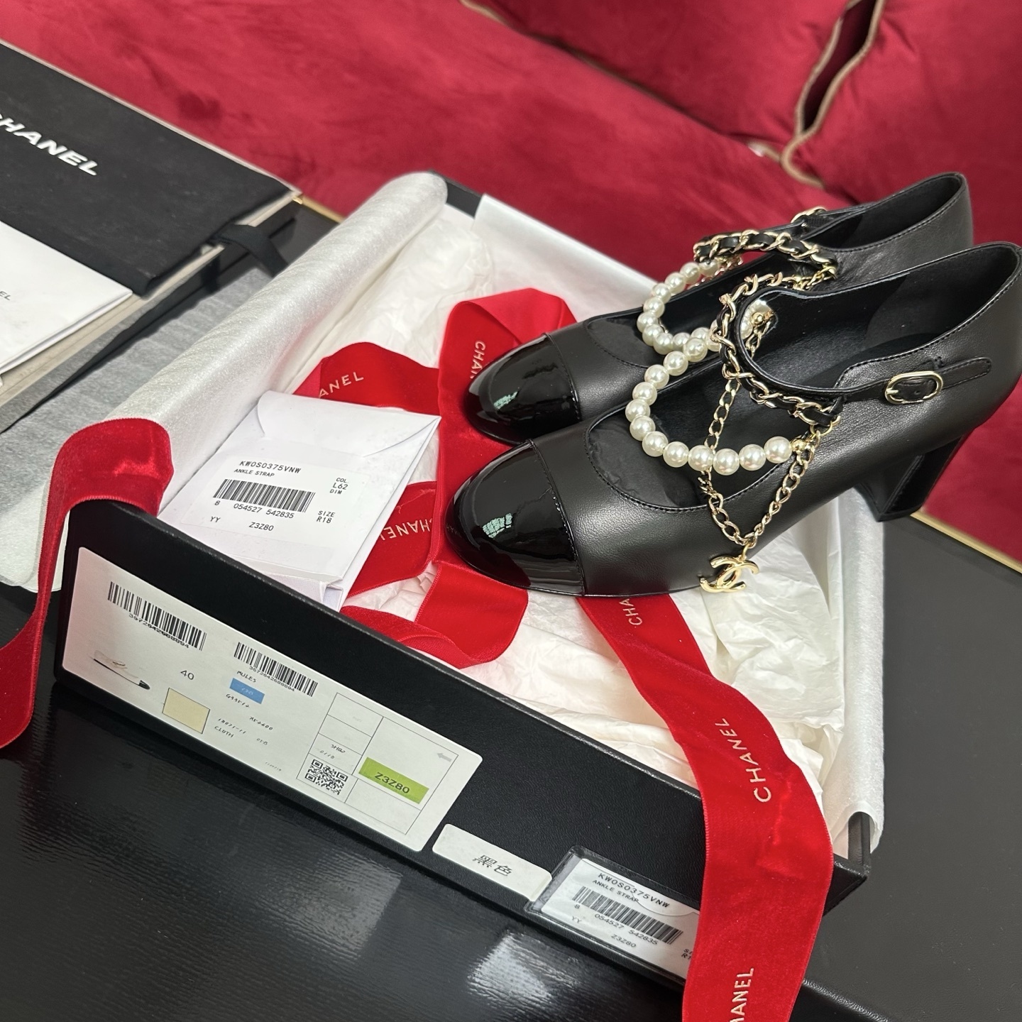 Luxury black Chanel Mary Jane pumps with patent leather cap toes and decorative pearl and gold chain straps displayed in a branded box. - Hình 2