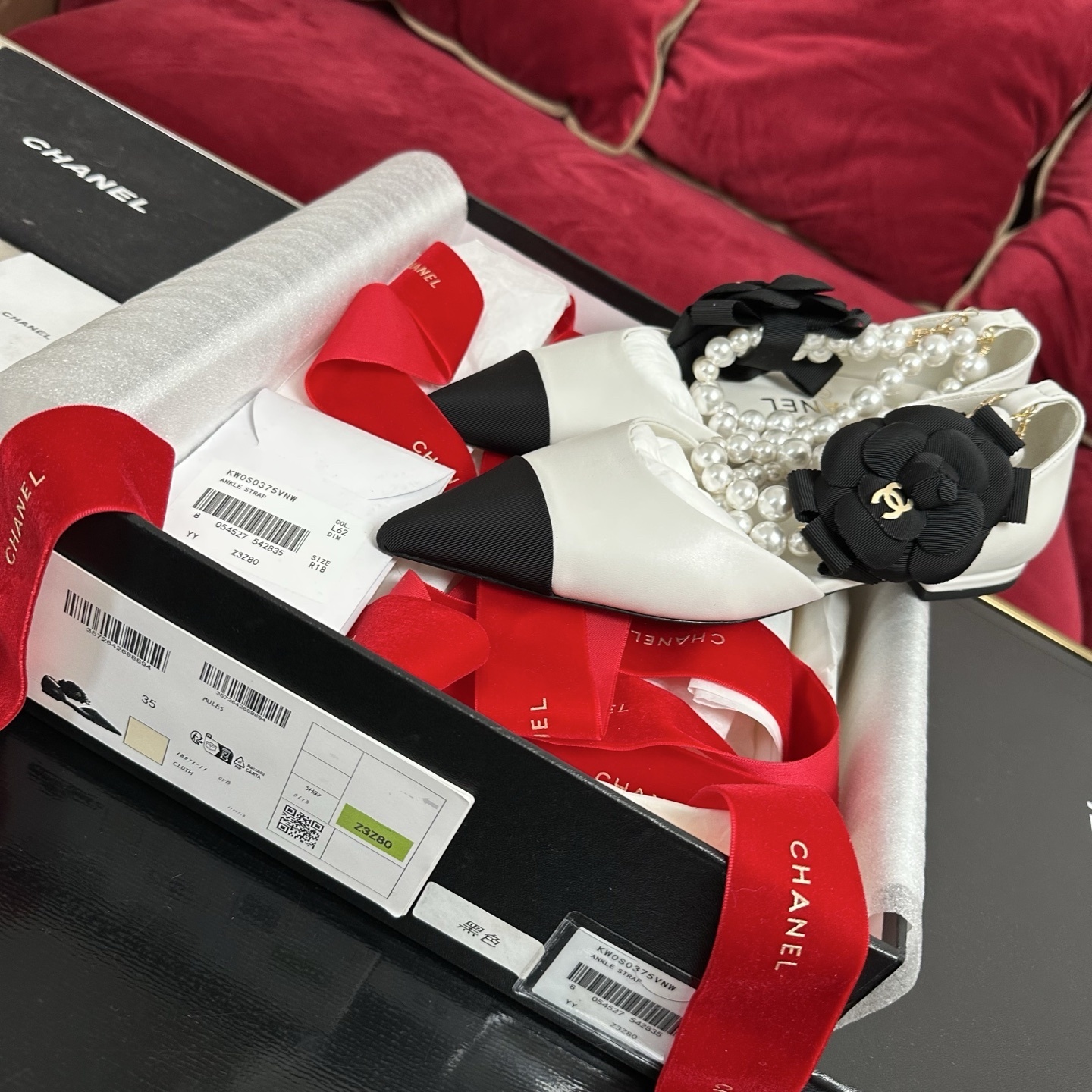 Chanel white leather mules with black cap toe, pearl ankle strap, and black camellia flower charm in original packaging. - Hình 2