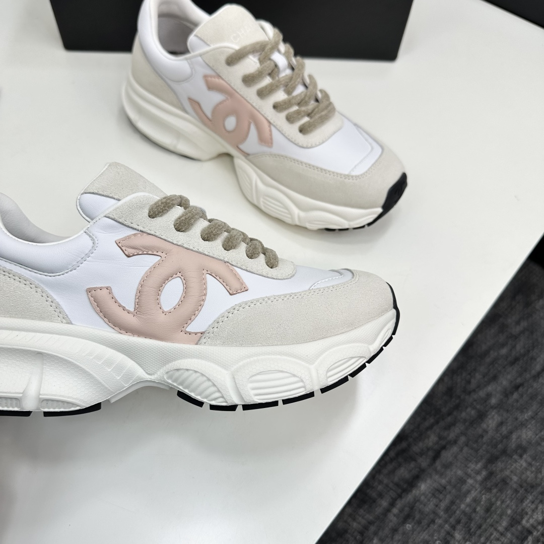 A pair of Chanel chunky sneakers in white leather and cream suede featuring a pink CC logo on the side, displayed on a black box. - Hình 2