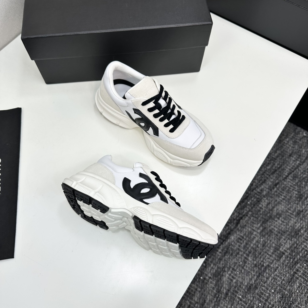 Side view of white and cream Chanel sneakers with black CC logo and chunky soles on a black luxury box - Hình 10