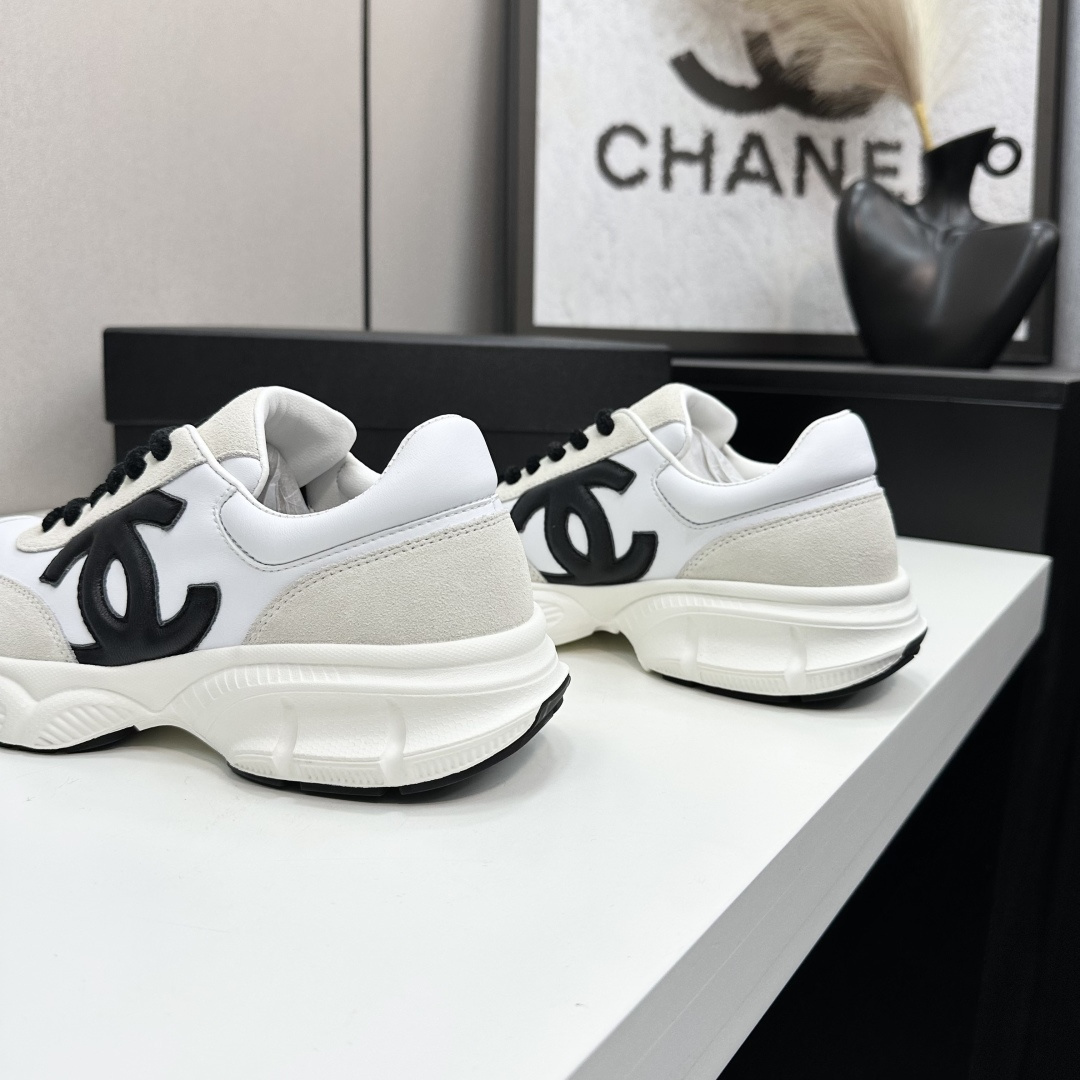 Side view of white and cream Chanel sneakers with black CC logo and chunky soles on a black luxury box - Hình 9