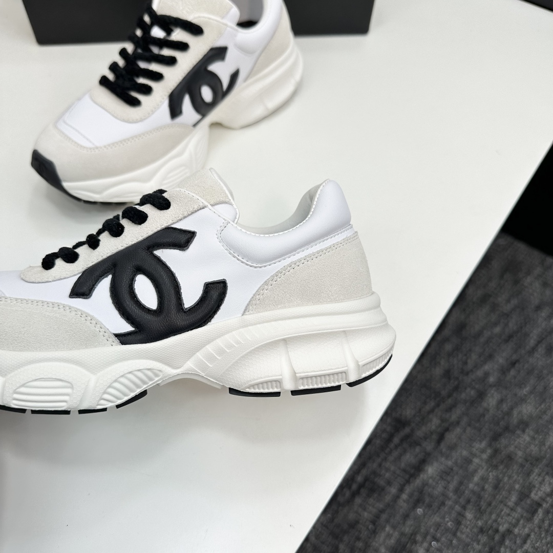 Side view of white and cream Chanel sneakers with black CC logo and chunky soles on a black luxury box - Hình 8
