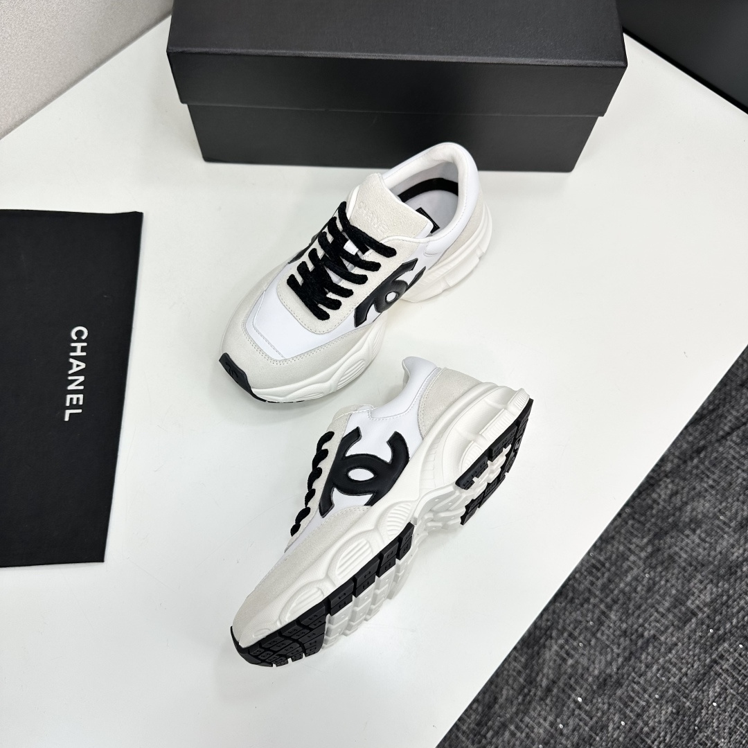 Side view of white and cream Chanel sneakers with black CC logo and chunky soles on a black luxury box - Hình 7