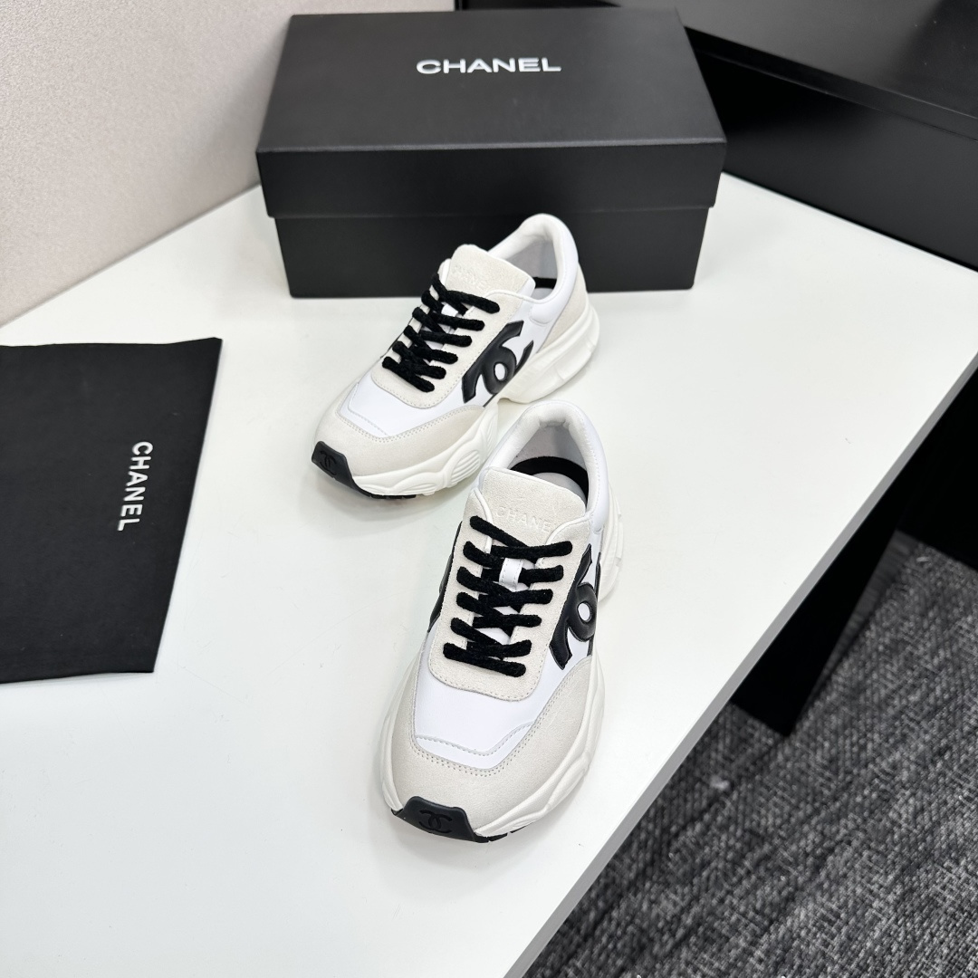 Side view of white and cream Chanel sneakers with black CC logo and chunky soles on a black luxury box - Hình 6