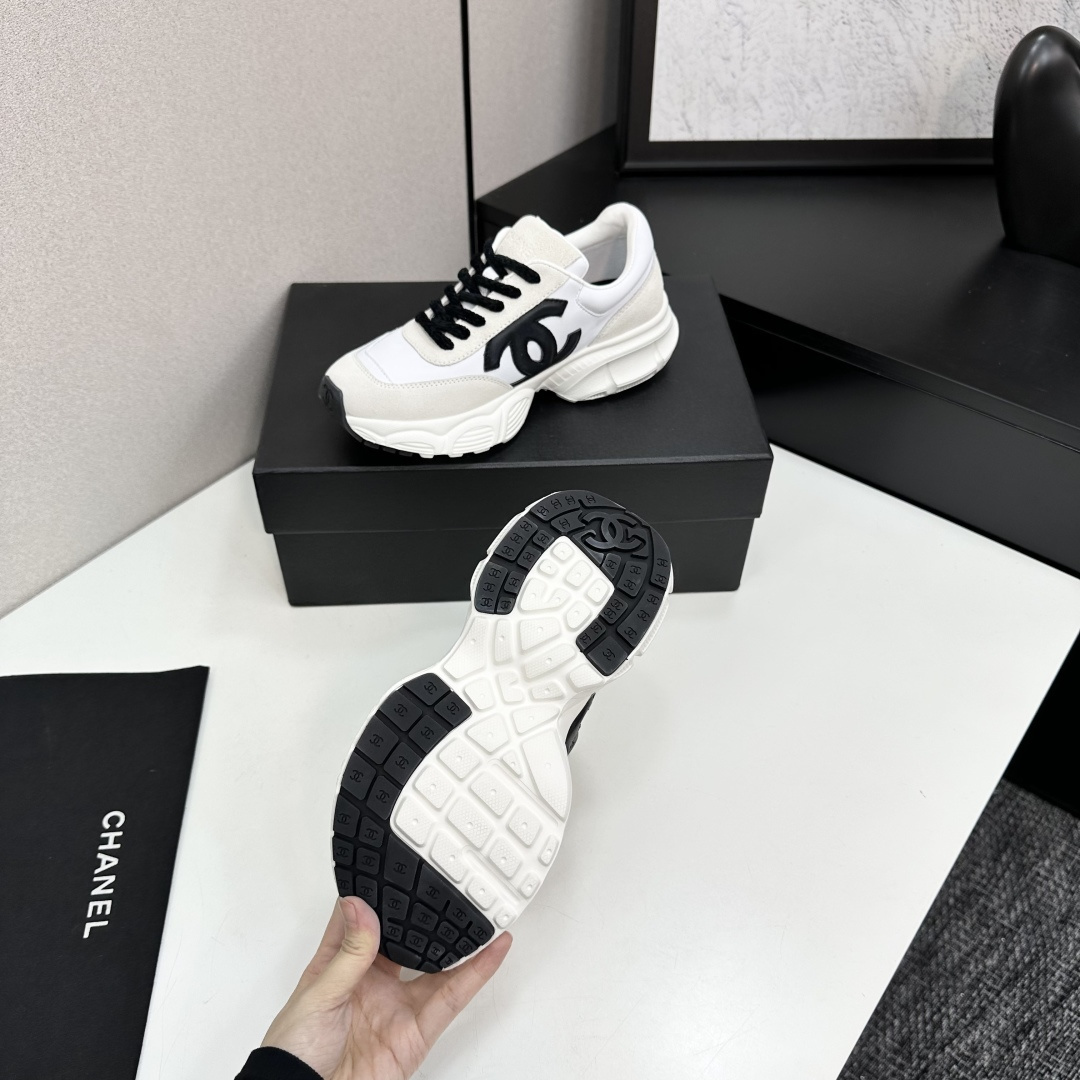 Side view of white and cream Chanel sneakers with black CC logo and chunky soles on a black luxury box - Hình 5