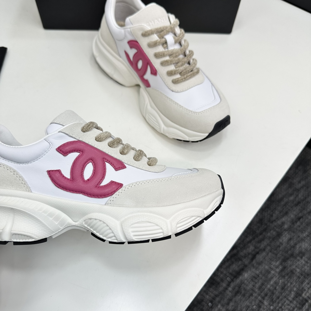 Side view of white and cream Chanel sneakers with a pink CC logo and chunky white soles on a black box. - Hình 2