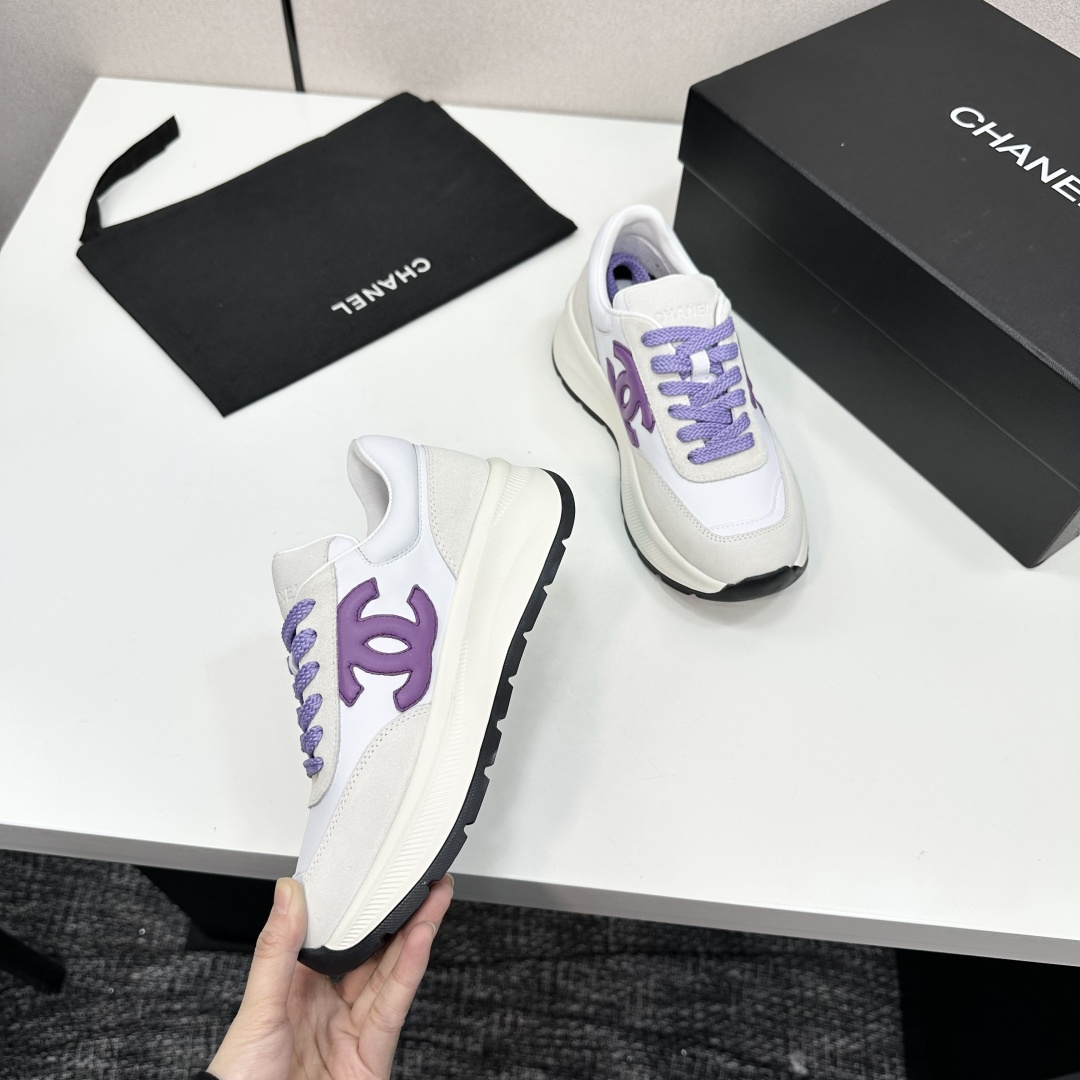 A pair of Chanel sneakers in white leather and grey suede with purple CC logo and laces on a black designer box. - Hình 2