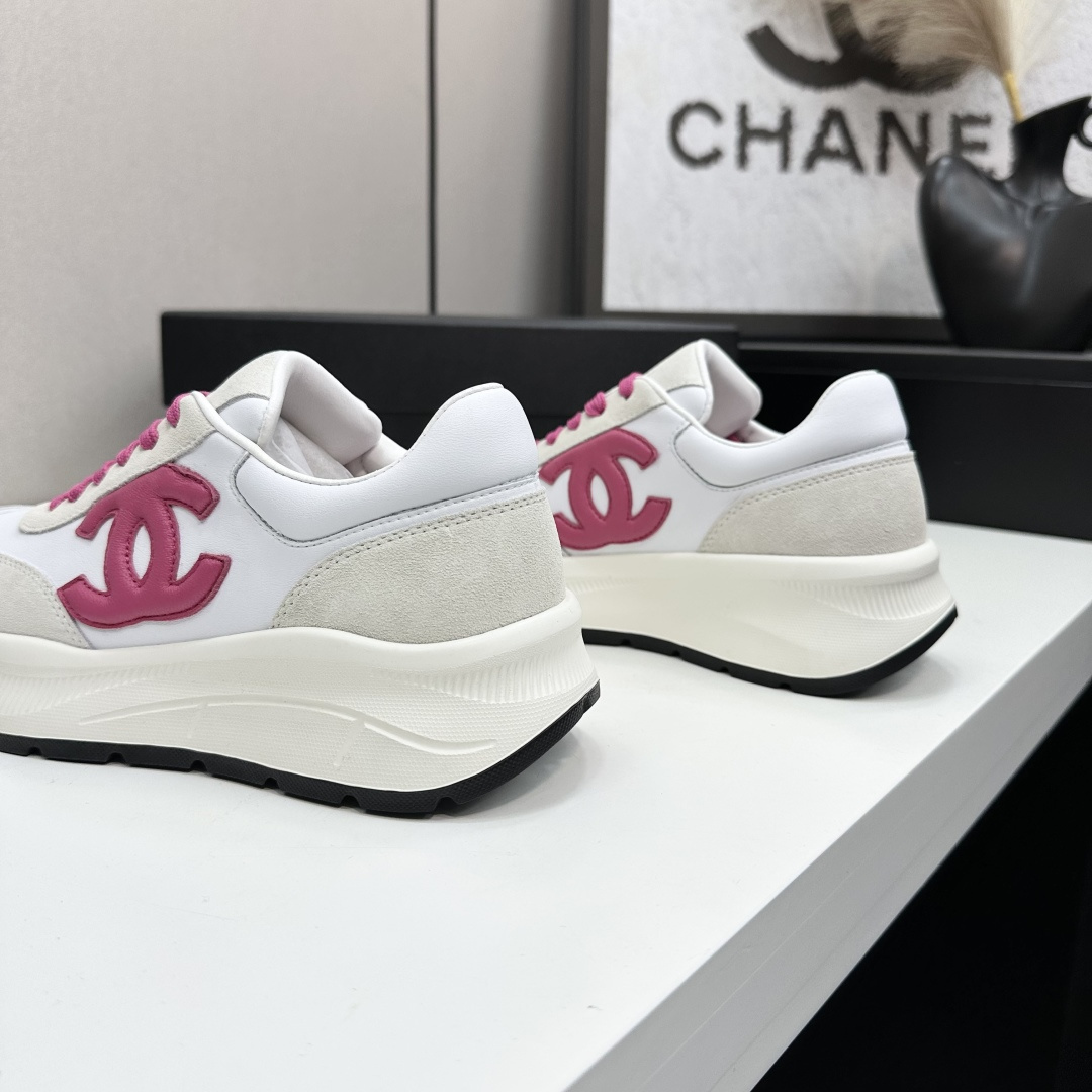 A pair of white and beige Chanel sneakers with a prominent pink CC logo and pink laces, displayed on a black box. - Hình 7