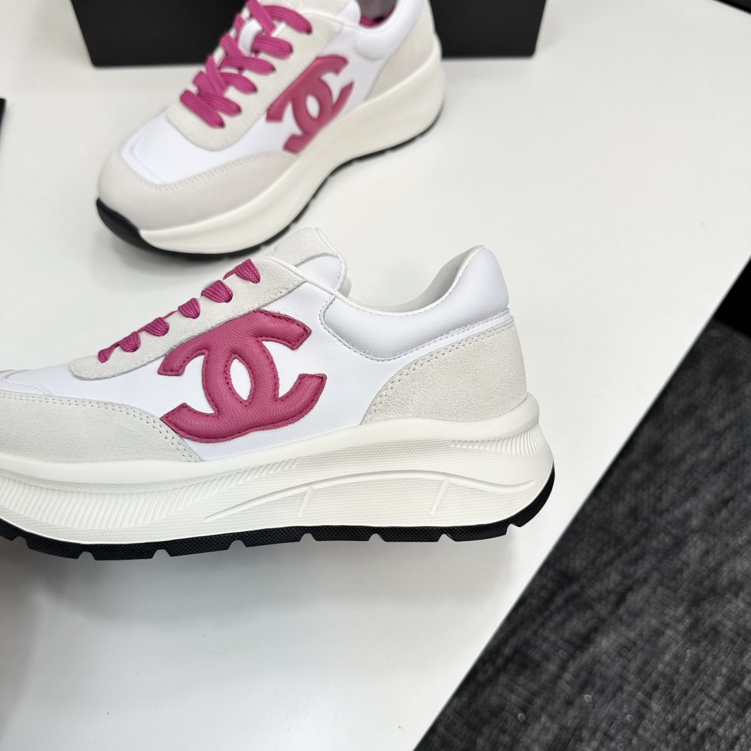 A pair of white and beige Chanel sneakers with a prominent pink CC logo and pink laces, displayed on a black box. - Hình 6
