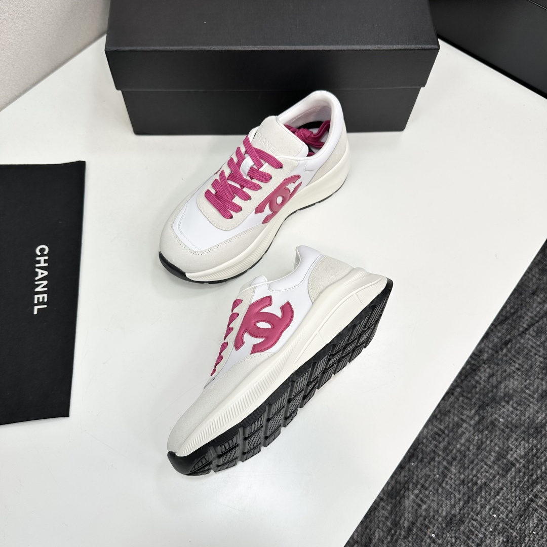 A pair of white and beige Chanel sneakers with a prominent pink CC logo and pink laces, displayed on a black box. - Hình 5