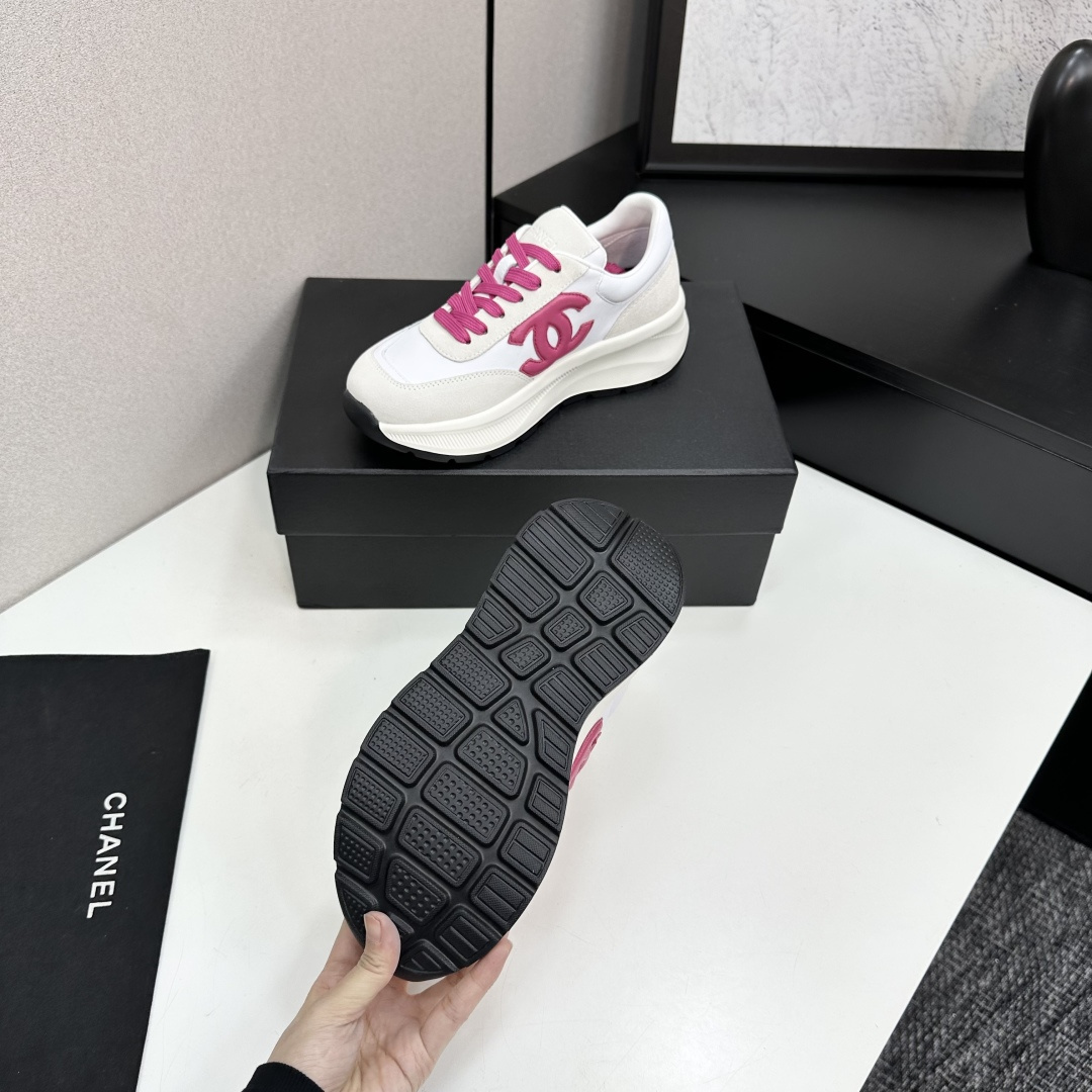 A pair of white and beige Chanel sneakers with a prominent pink CC logo and pink laces, displayed on a black box. - Hình 4