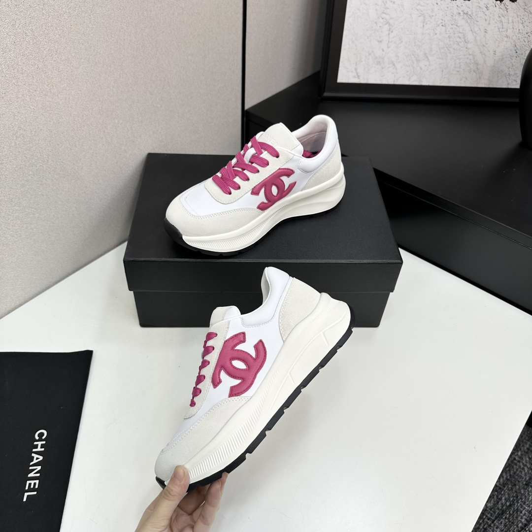 A pair of white and beige Chanel sneakers with a prominent pink CC logo and pink laces, displayed on a black box. - Hình 3