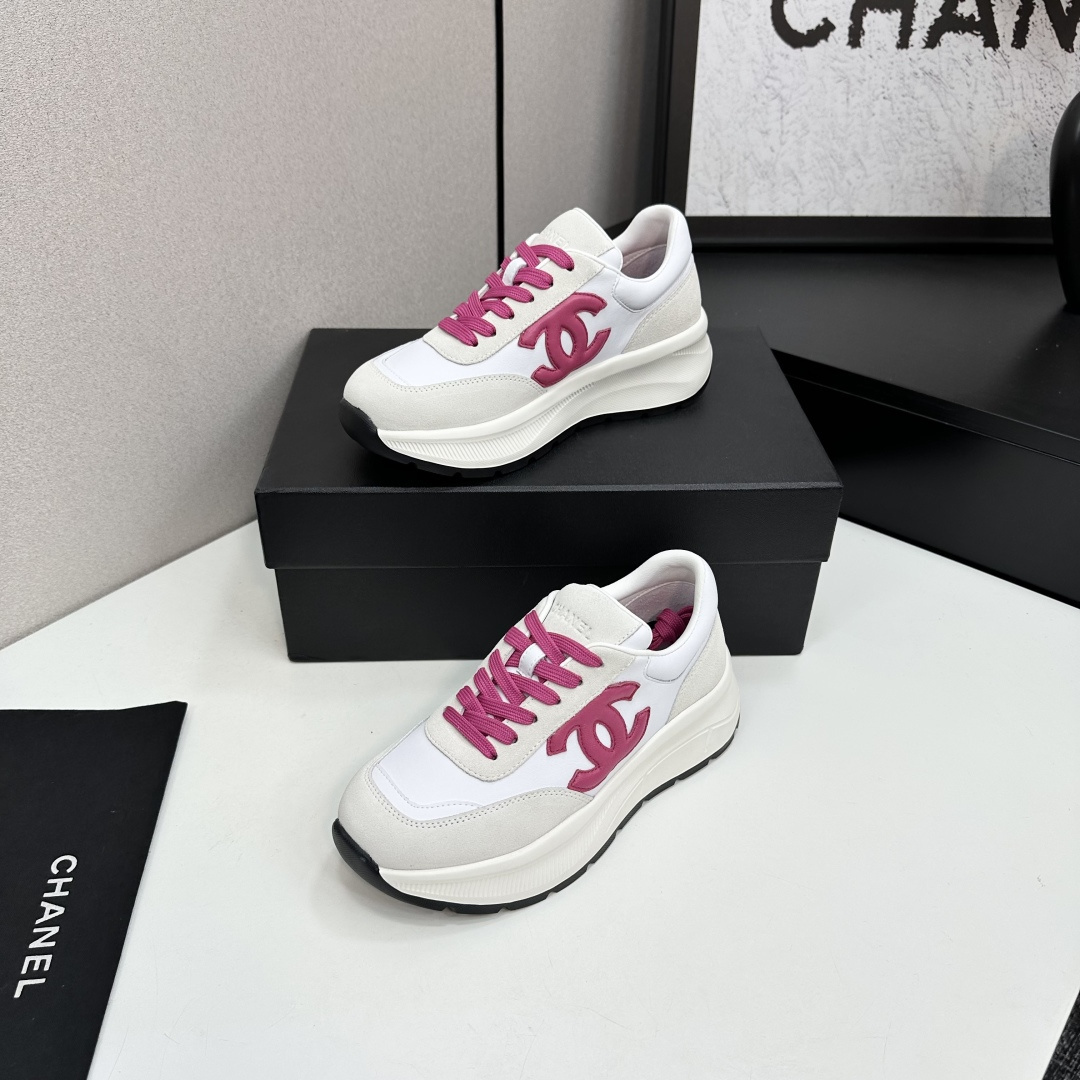 A pair of white and beige Chanel sneakers with a prominent pink CC logo and pink laces, displayed on a black box. - Hình 2