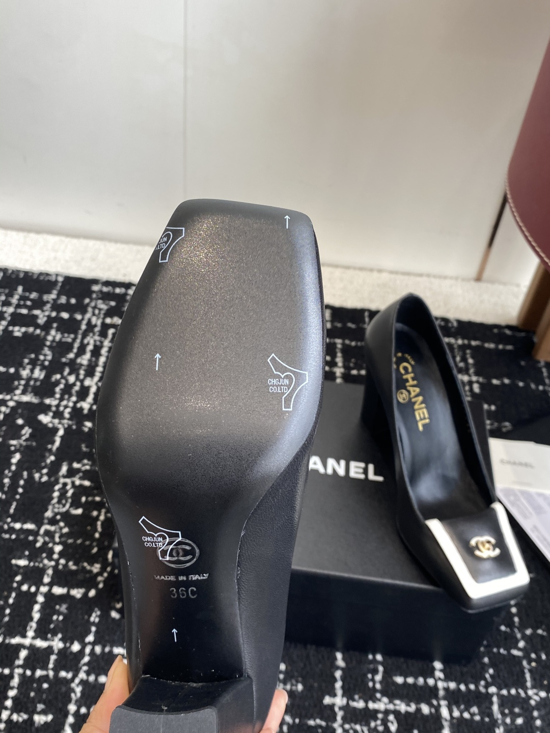 Chanel black leather square toe pumps with gold CC logo and white trim detail on a luxury shoe box - Hình 9