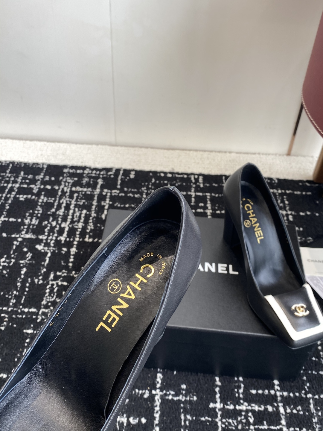 Chanel black leather square toe pumps with gold CC logo and white trim detail on a luxury shoe box - Hình 7