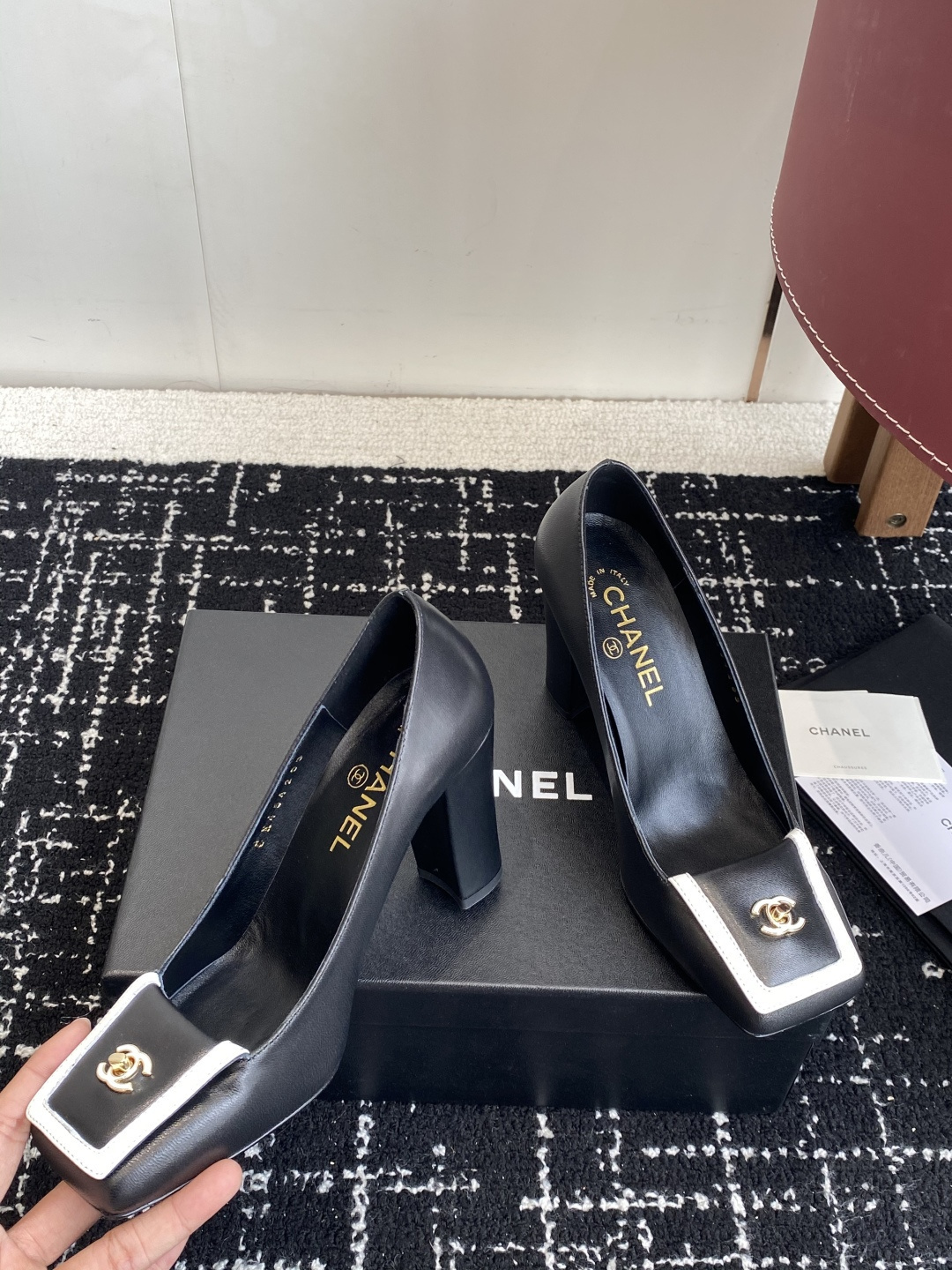 Chanel black leather square toe pumps with gold CC logo and white trim detail on a luxury shoe box - Hình 6