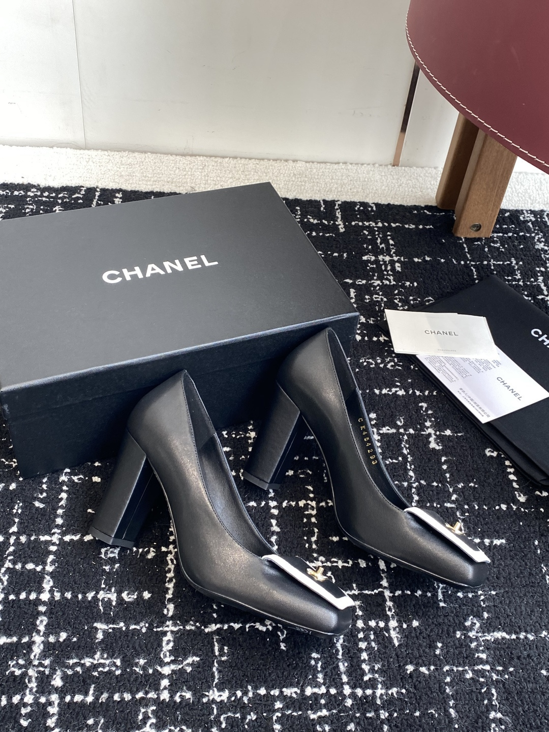 Chanel black leather square toe pumps with gold CC logo and white trim detail on a luxury shoe box - Hình 4