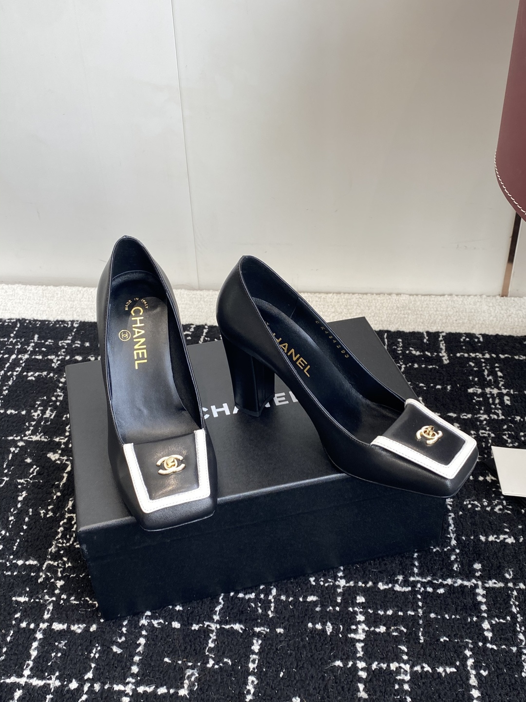 Chanel black leather square toe pumps with gold CC logo and white trim detail on a luxury shoe box - Hình 3
