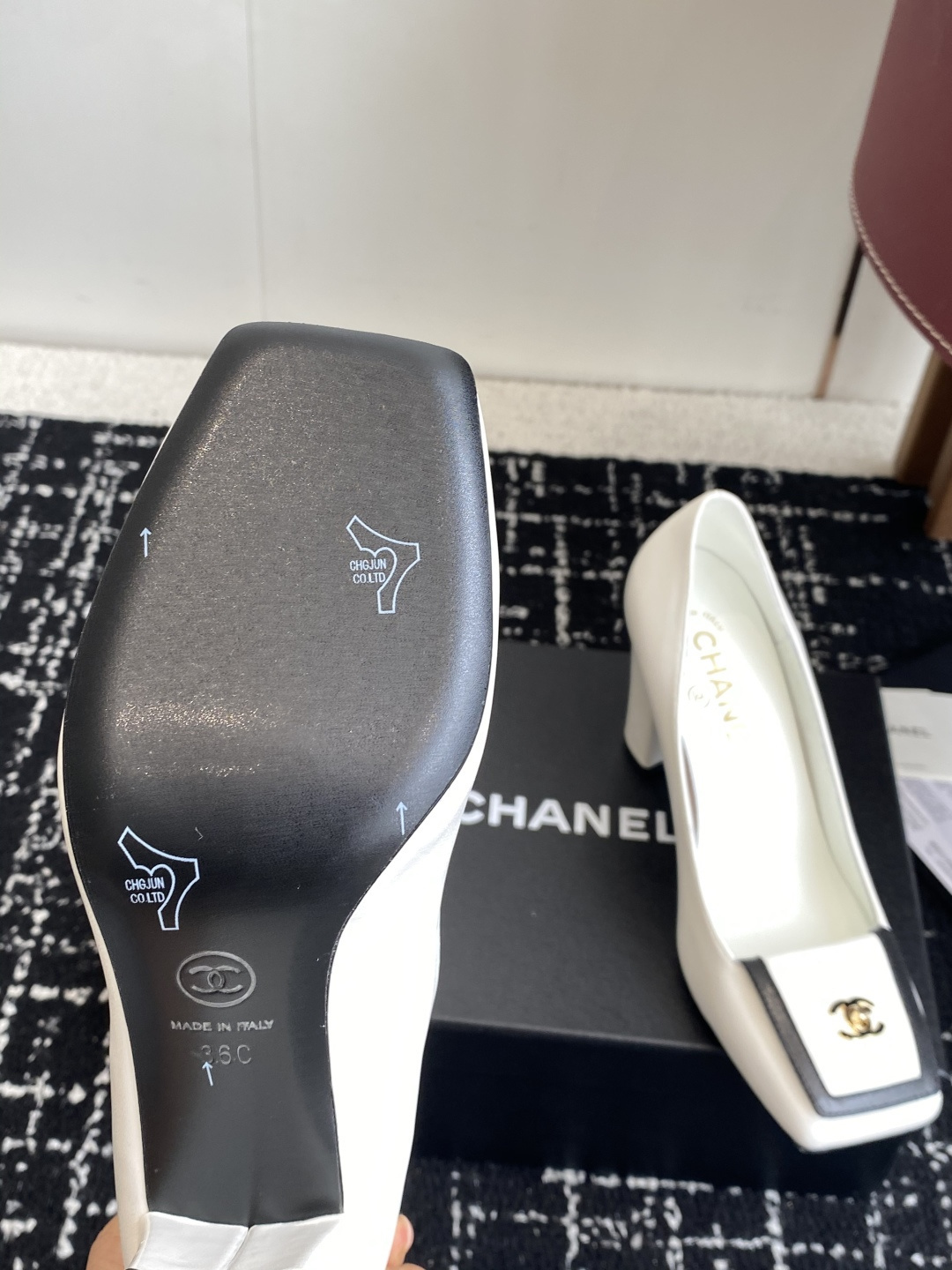 Chanel white leather pumps with black trim, gold CC logo, and block heels on a black box. - Hình 9