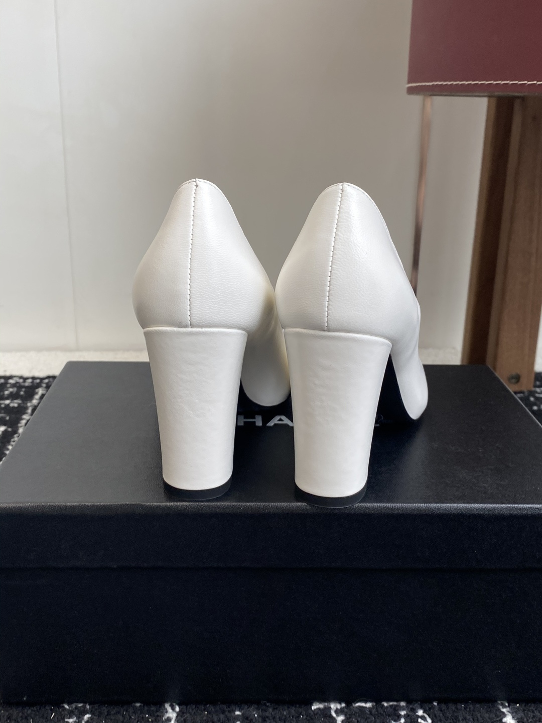 Chanel white leather pumps with black trim, gold CC logo, and block heels on a black box. - Hình 8