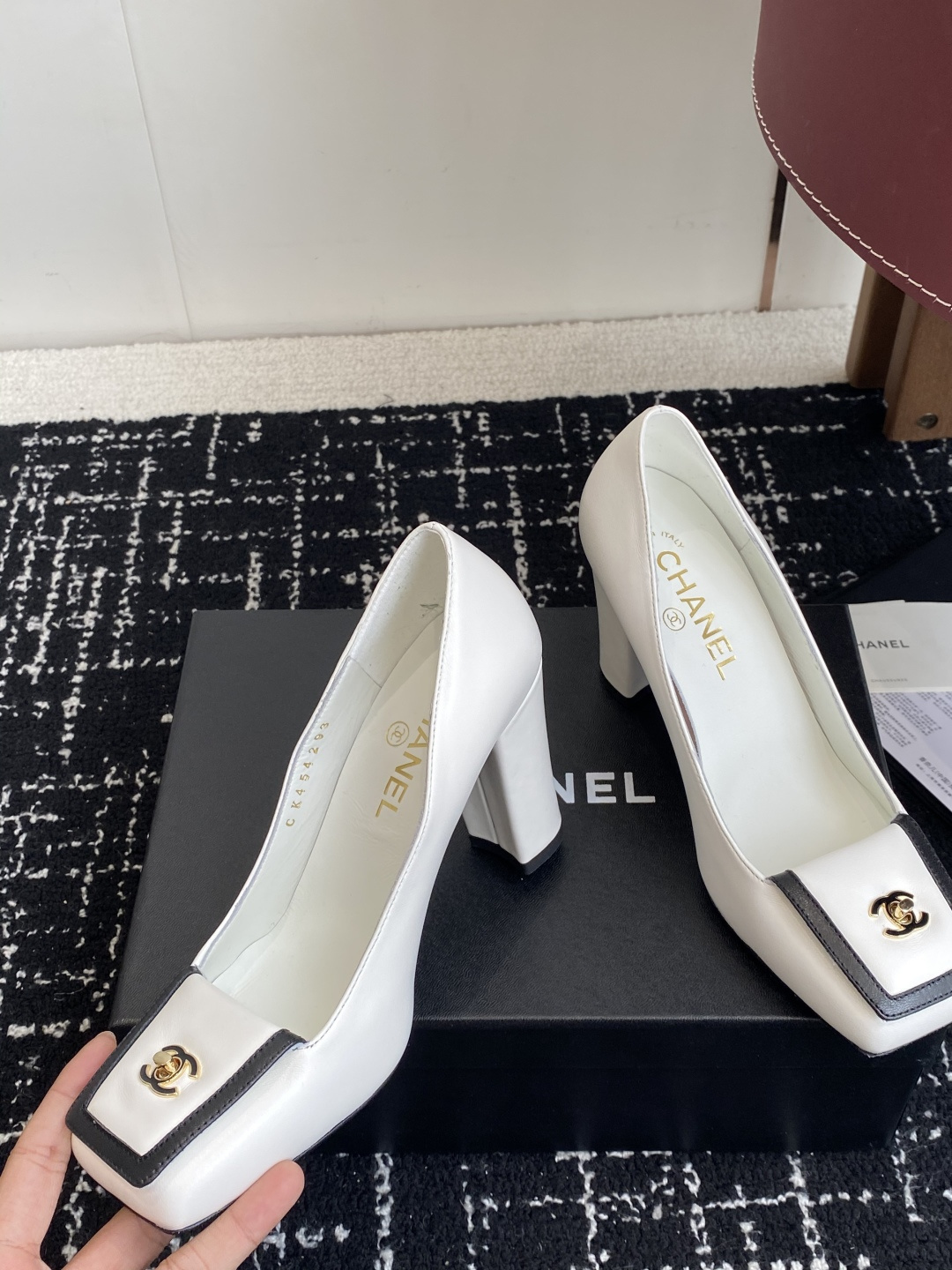 Chanel white leather pumps with black trim, gold CC logo, and block heels on a black box. - Hình 6