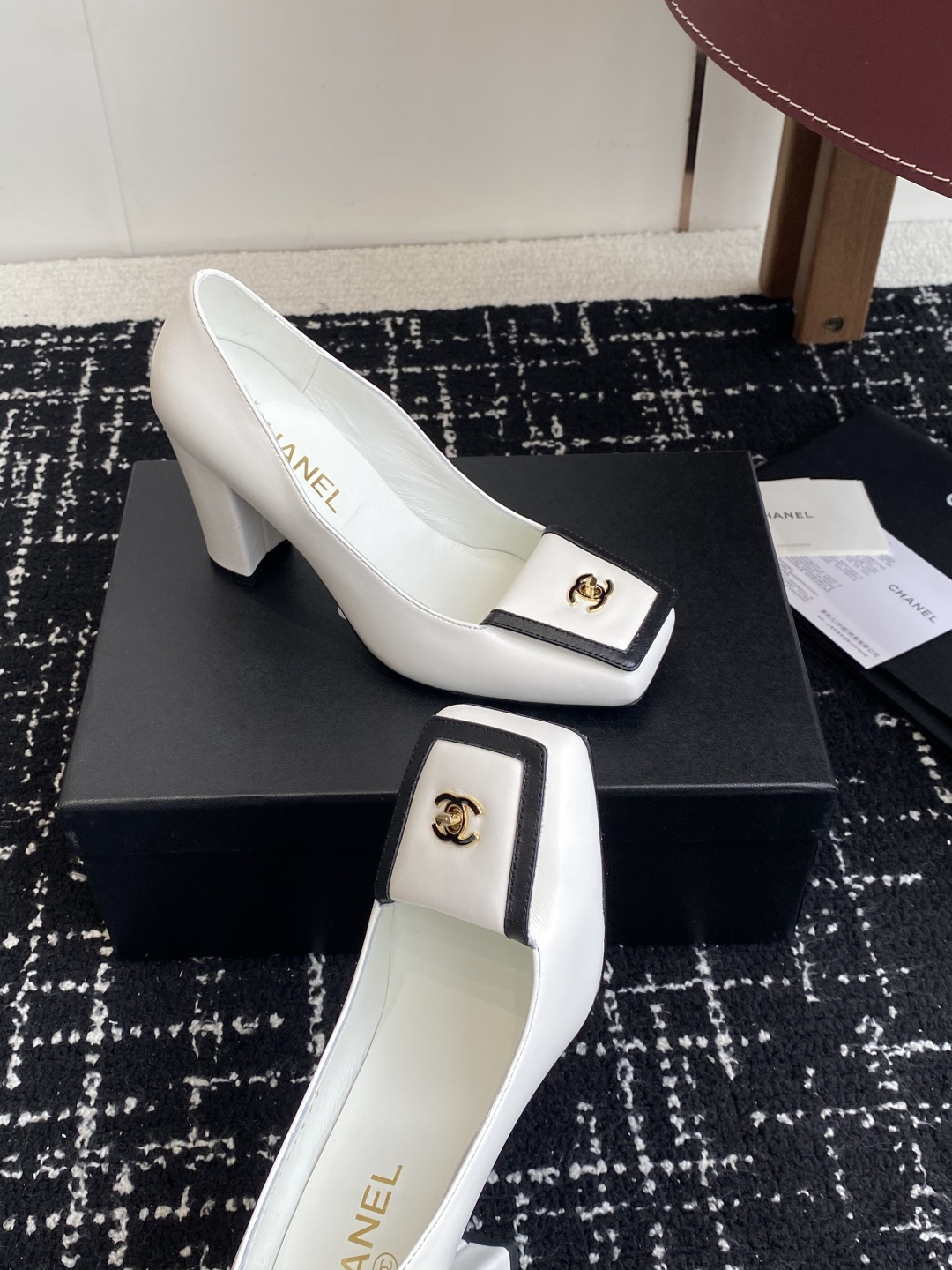 Chanel white leather pumps with black trim, gold CC logo, and block heels on a black box. - Hình 5