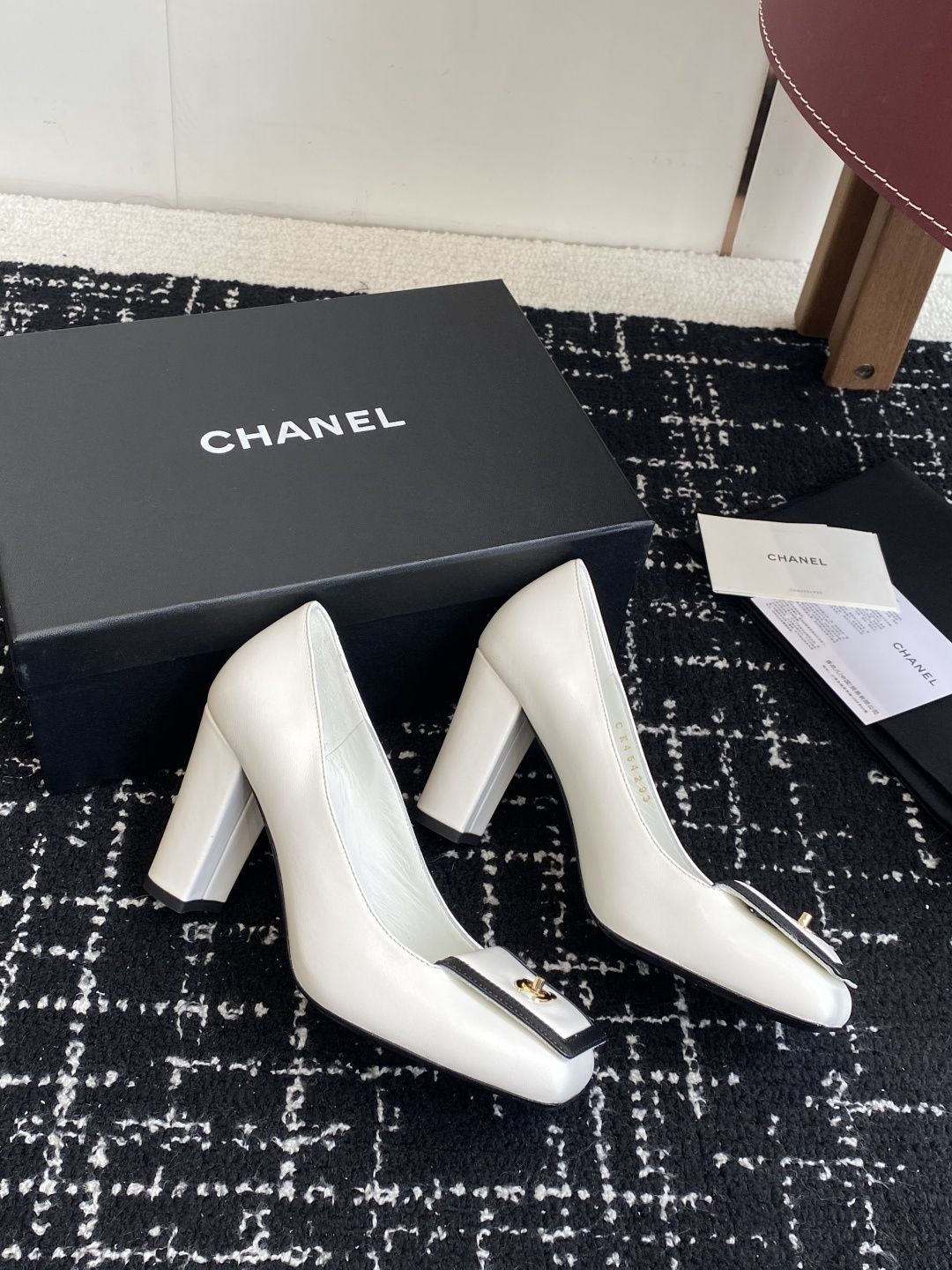 Chanel white leather pumps with black trim, gold CC logo, and block heels on a black box. - Hình 4