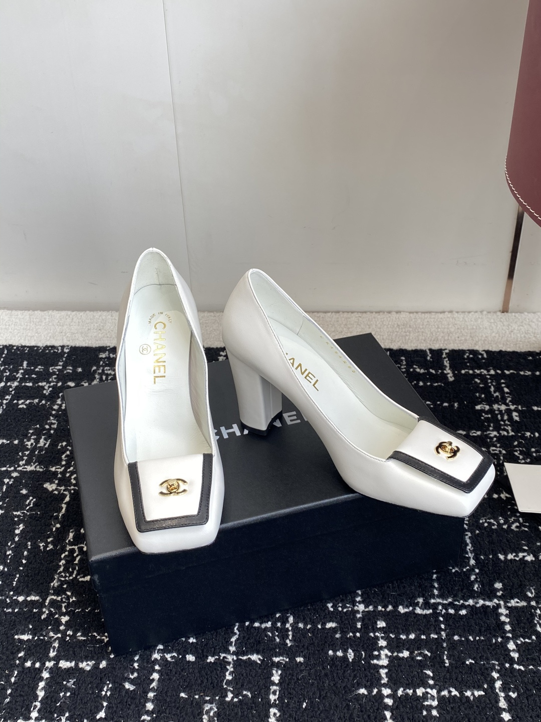 Chanel white leather pumps with black trim, gold CC logo, and block heels on a black box. - Hình 3