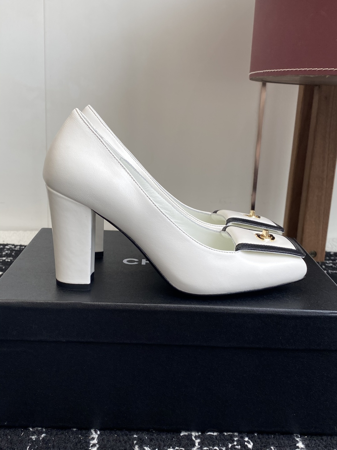 Chanel white leather pumps with black trim, gold CC logo, and block heels on a black box. - Hình 2