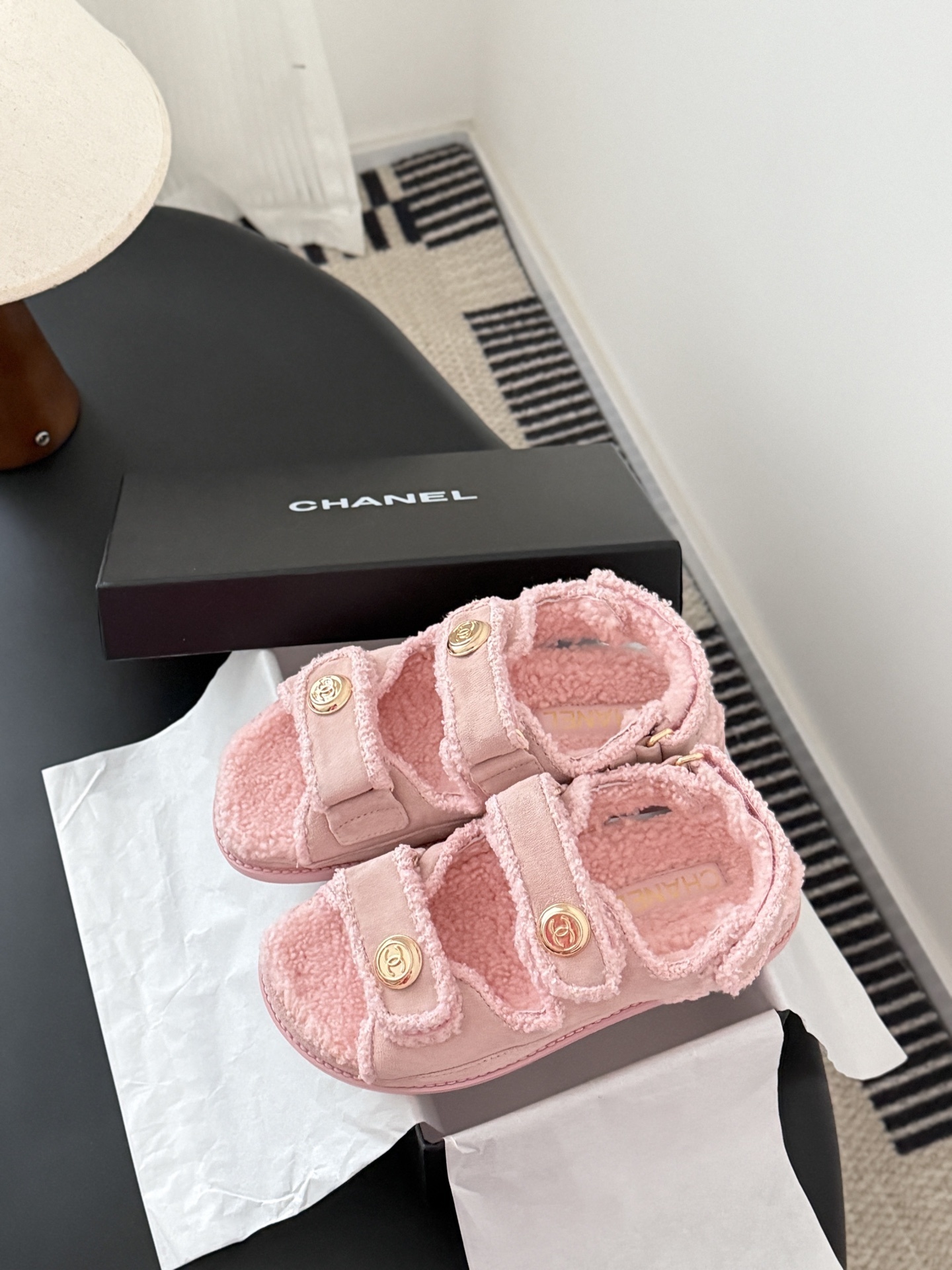Pair of pink Chanel shearling sandals with gold CC logo buttons sitting next to a black Chanel box. - Hình 9